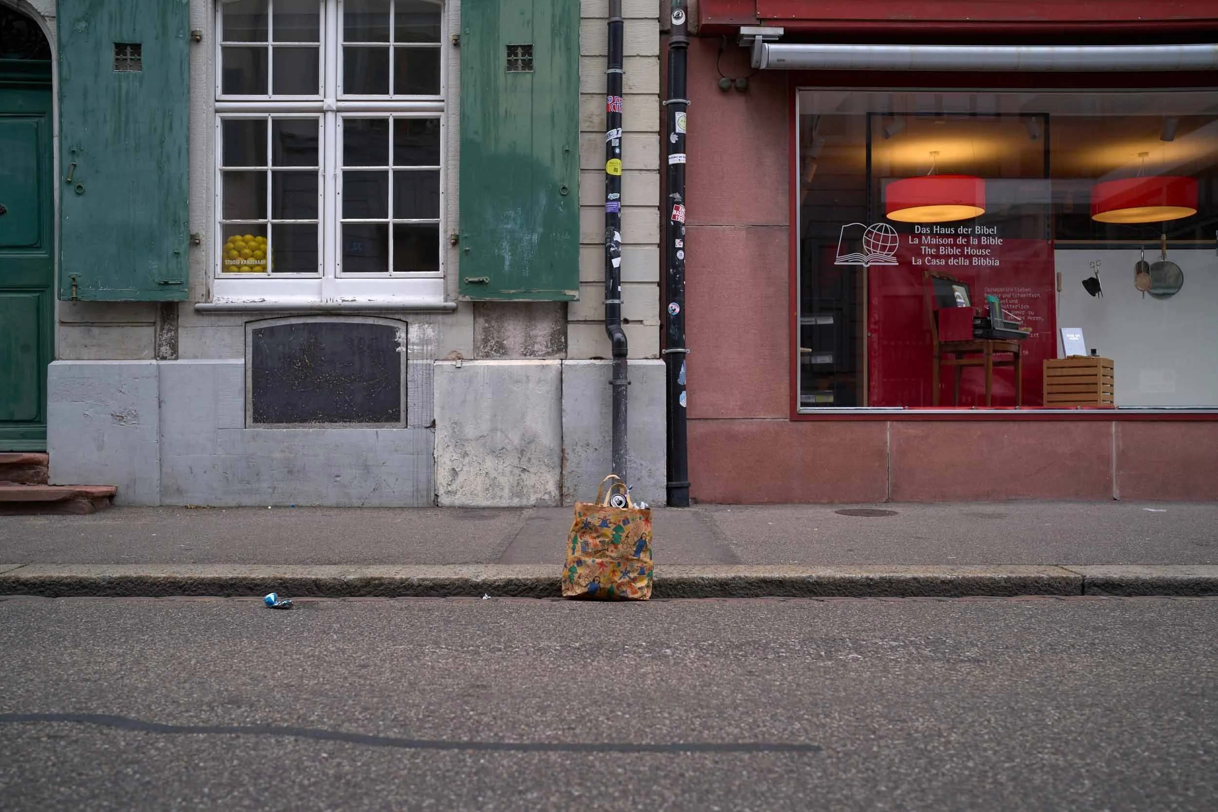 Eine Einkaufstasche steht am Strassenrand vor Gebäuden mit Schaufenstern.