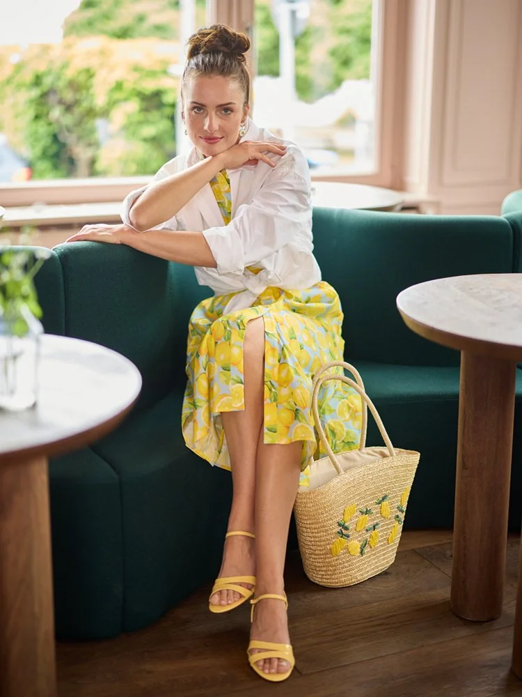 Frau mit Zitronenkleid und weißer Bluse sitzend im Café mit Strohtasche