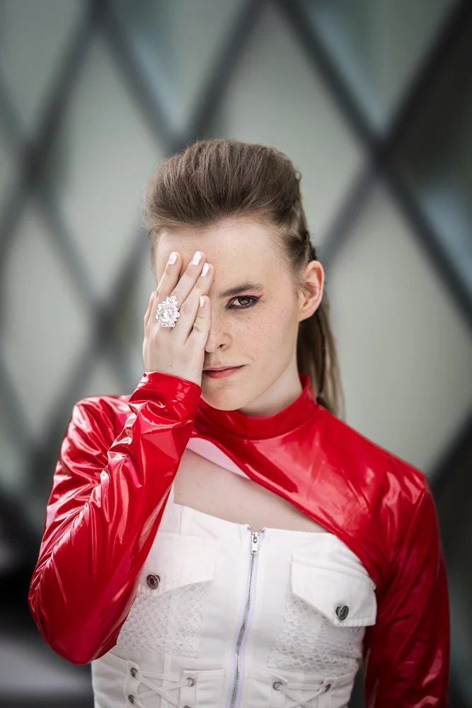 Porträt eines Bandmitglieds von III RIØT vor der Fassade des Futuriums in Berlin. Eine Hand verdeckt ein Auge.