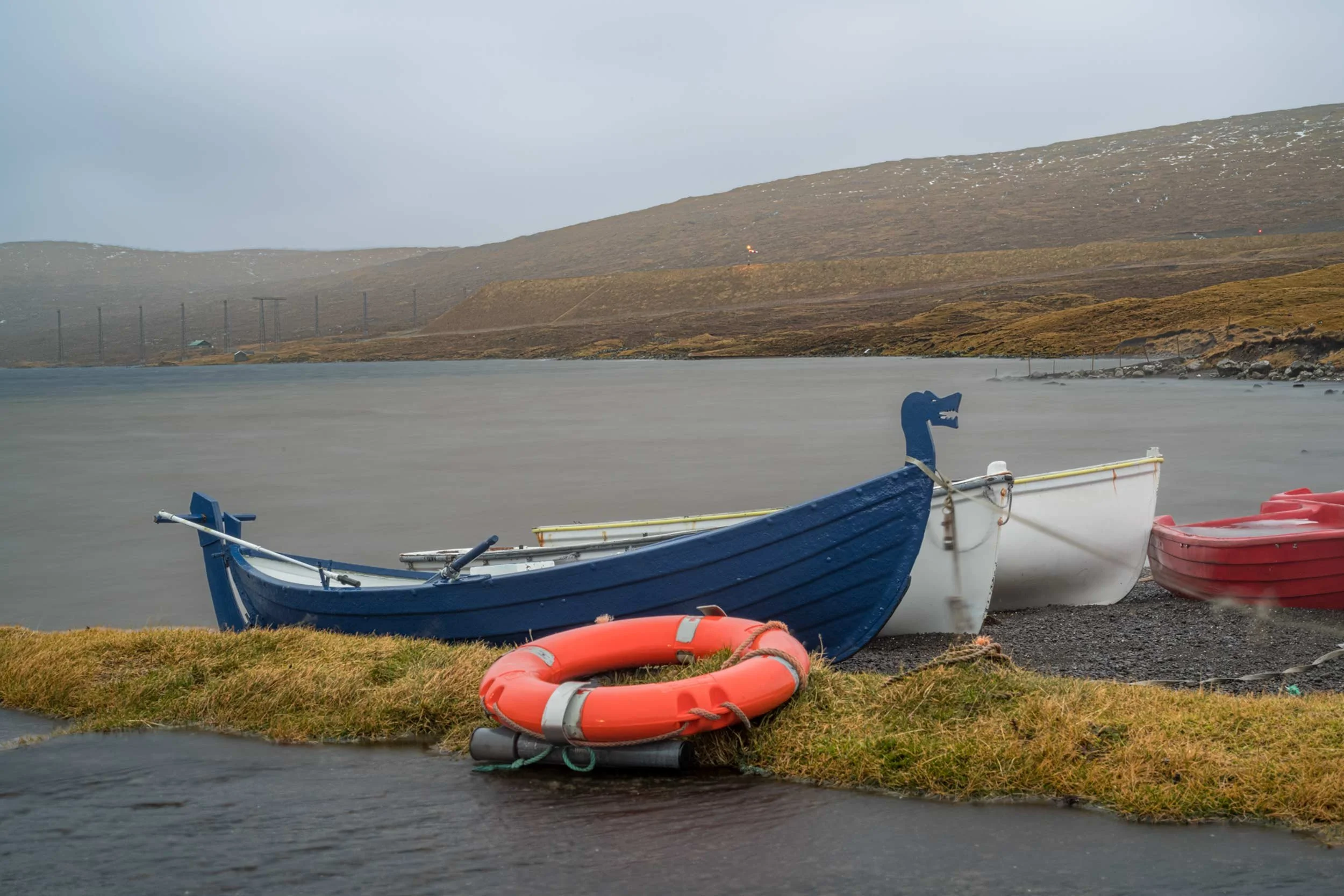 Blaues und weisses boot liegen am ufer eines sees, ein orangefarbener rettungsring liegt im vordergrund, faeroer