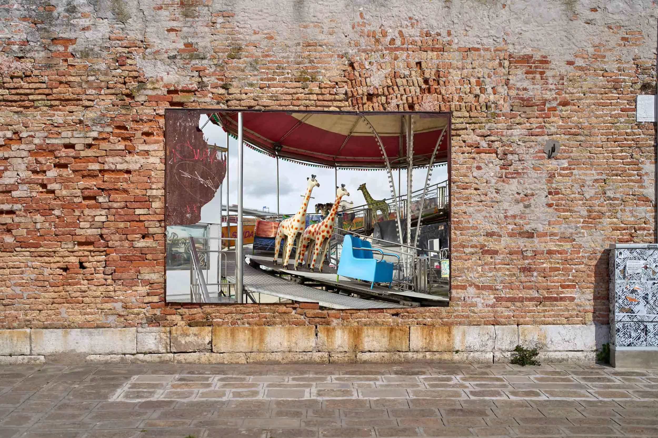 Framed photograph on a red brick wall in Venice, showing Mount Fuji behind a factory with smoking chimneys.