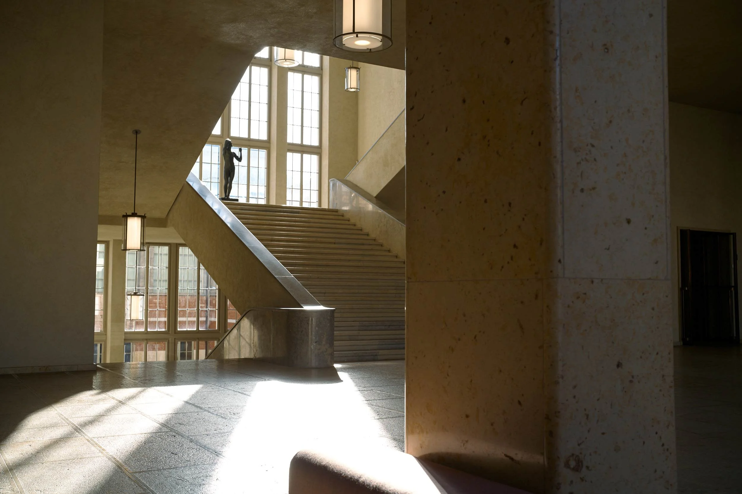 Treppenhaus im Kunst Museum Basel, oben steht eine Skulptur vor grossen Fenstern.