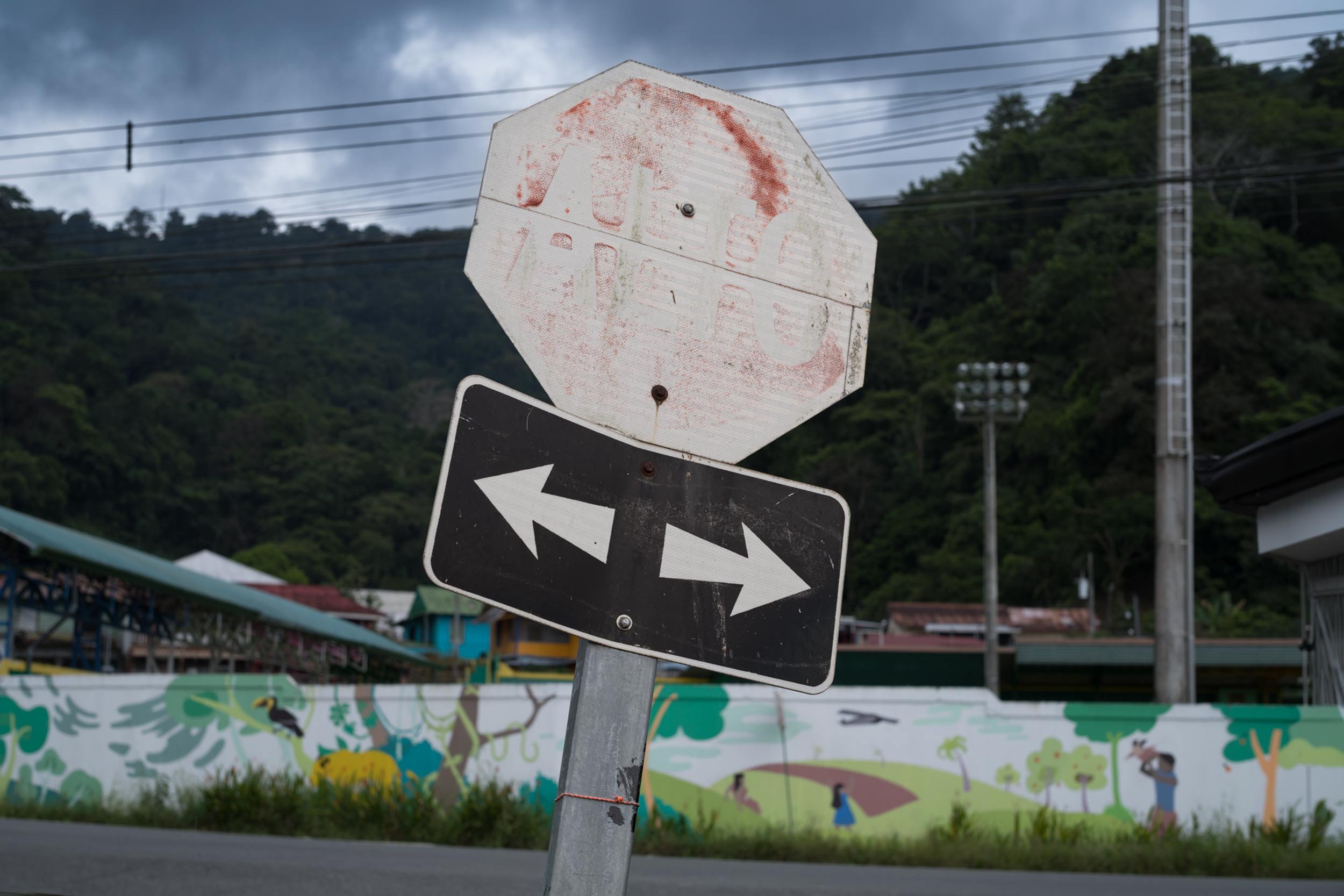 Verblasstes stoppschild mit darunter angebrachtem richtungsschild mit zwei pfeilen vor waldhang in costa rica