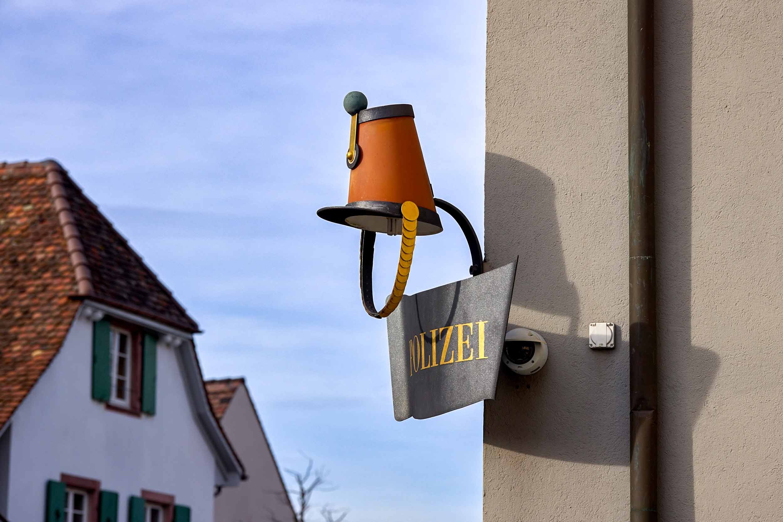 Ausleger mit der Aufschrift „Polizei“ und einer Lampe an der Fassade eines Gebäudes in einer Straße in Basel.