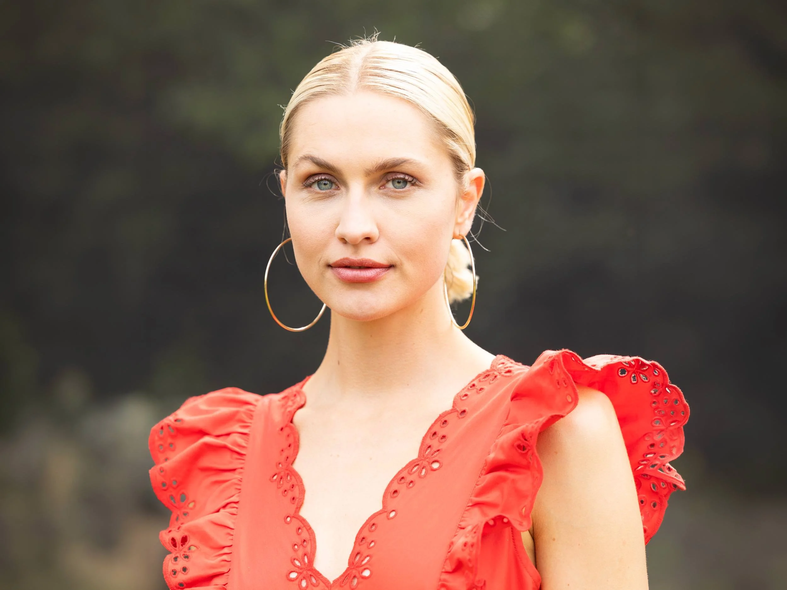 Frau mit rotem Kleid und großen Creolen blickt in die Kamera.