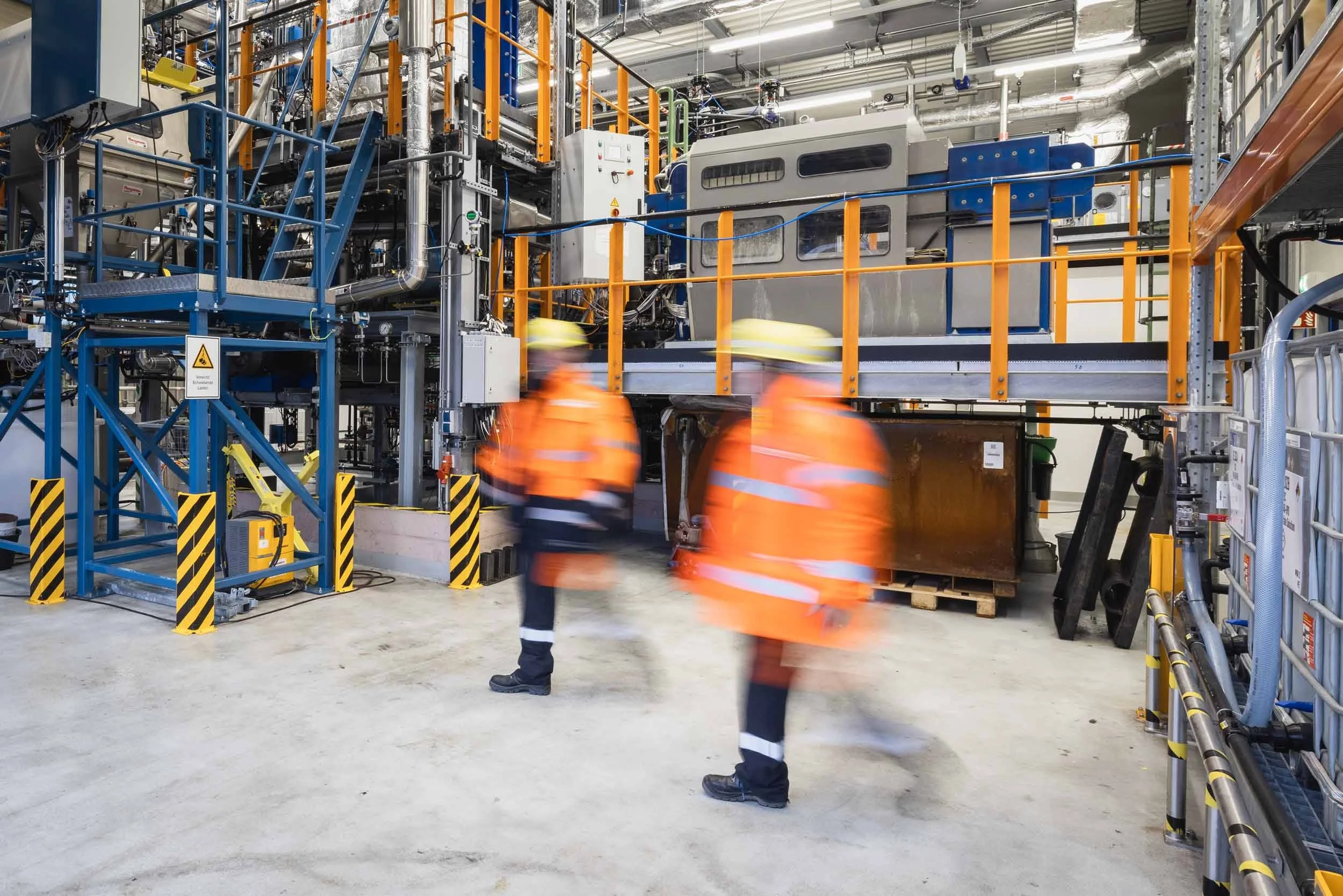 Zwei Fachkräfte in Bewegung innerhalb der Produktionshalle – industrielle Dynamik trifft auf strukturierte Techniklandschaft.