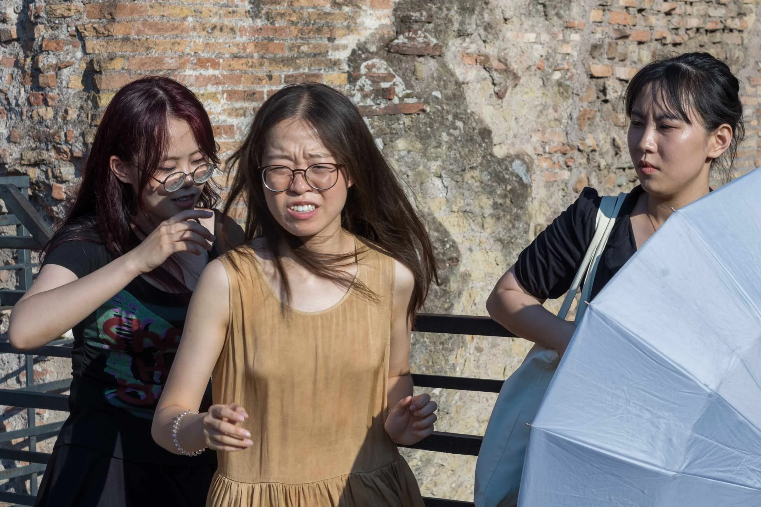 Drei Frauen stehen vor einer alten Ziegelmauer am Kolosseum in Rom, eine hält einen weißen Sonnenschirm.