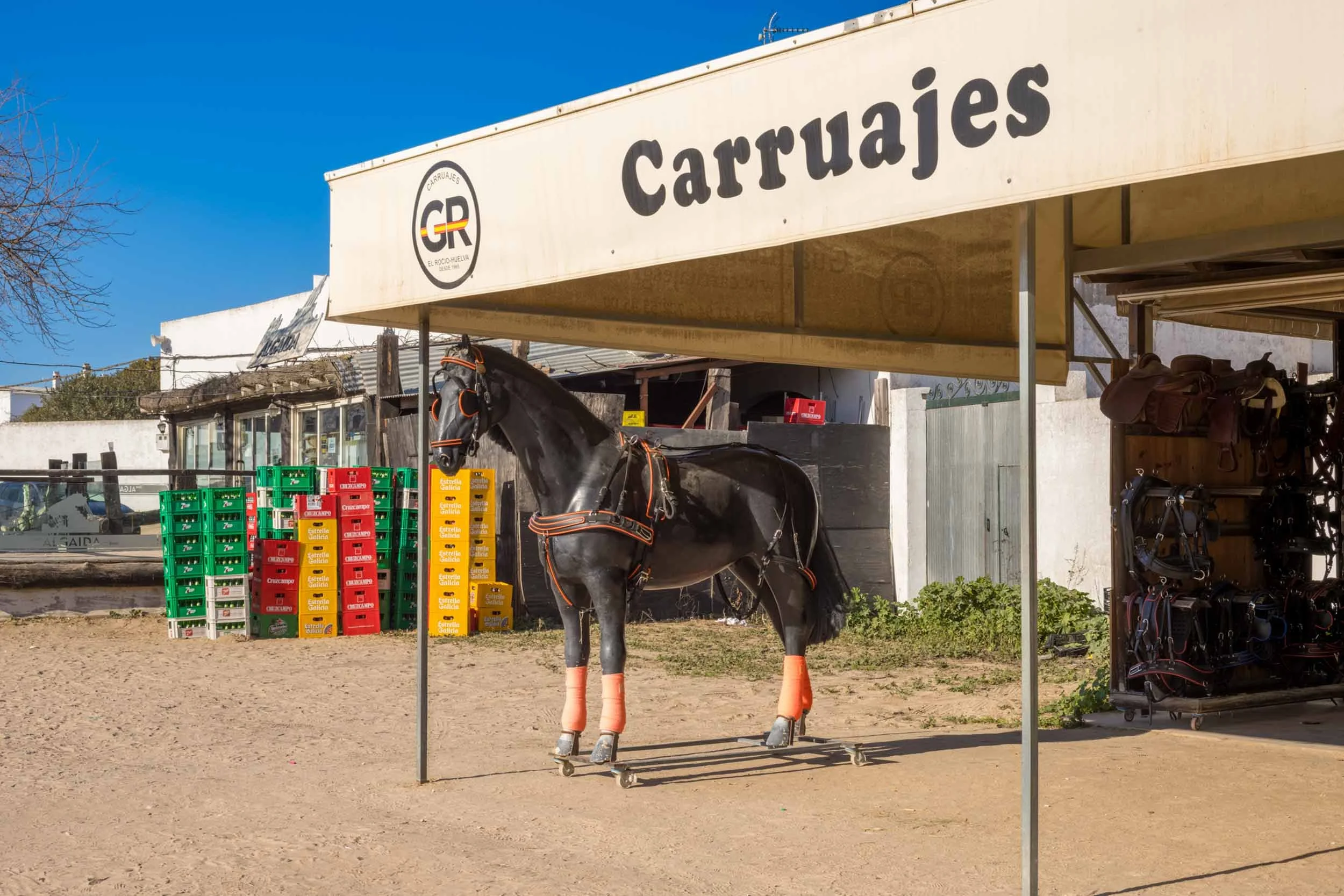 Schwarzes pferd mit geschirr steht unter einem unterstand mit der aufschrift carruajes in El Rocio