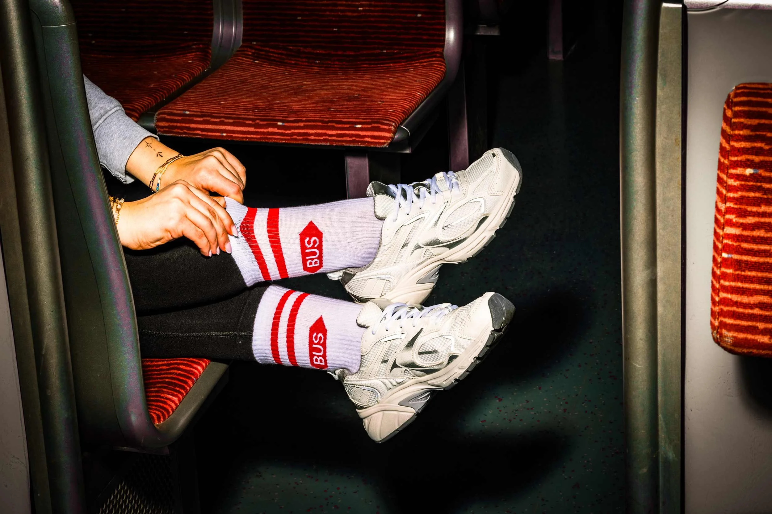 Detailaufnahme von weißen Sneakern und Hochbahn-Bus-Socken im Innenraum eines Fahrzeugs.