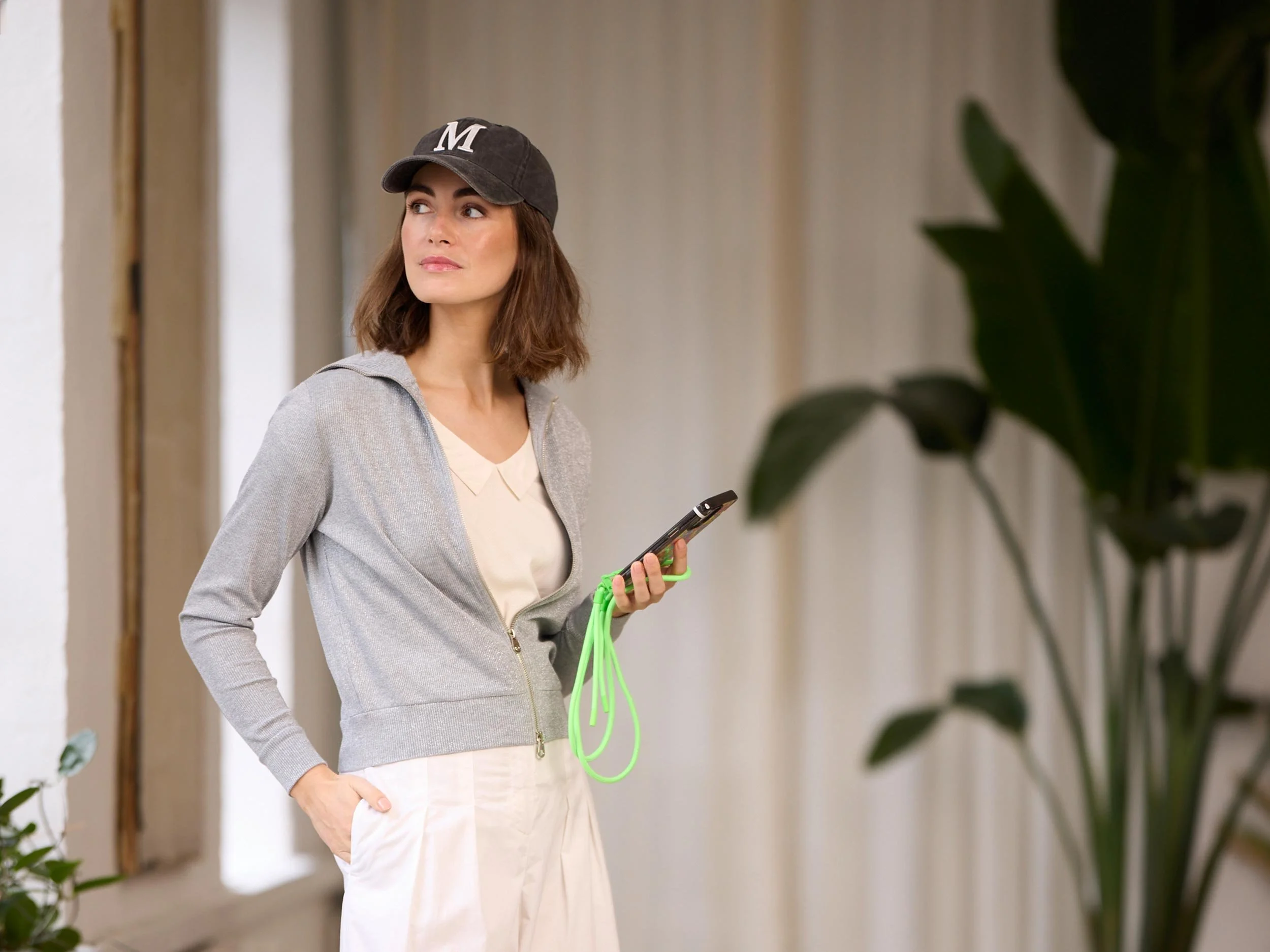 Frau mit dunkler Cap, grauer Jacke und Smartphone in modernem Innenraum