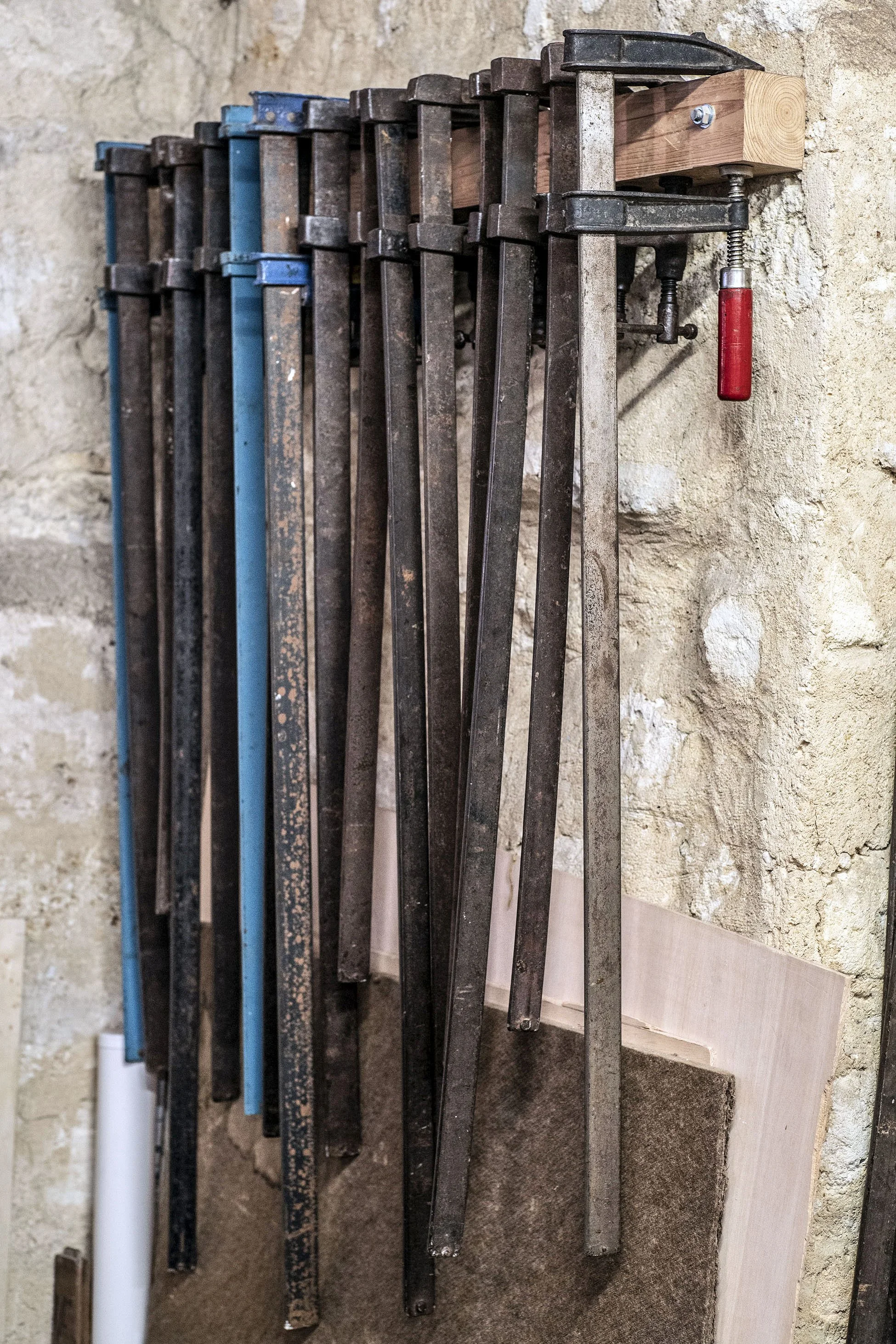 Barres en métal empilées contre un mur en pierre, utilisées pour la menuiserie, avec une pince enroulée attachée à une des barres.