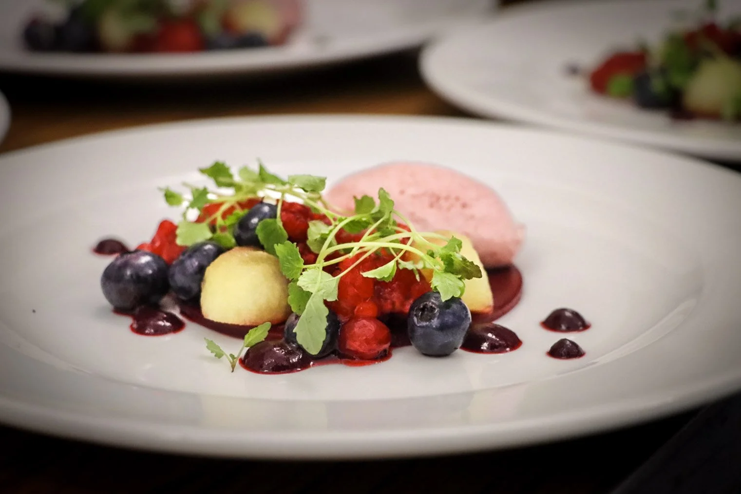 Plate of assorted fresh berries, sliced apple, and microgreens, with pink meringue and berry sauce.