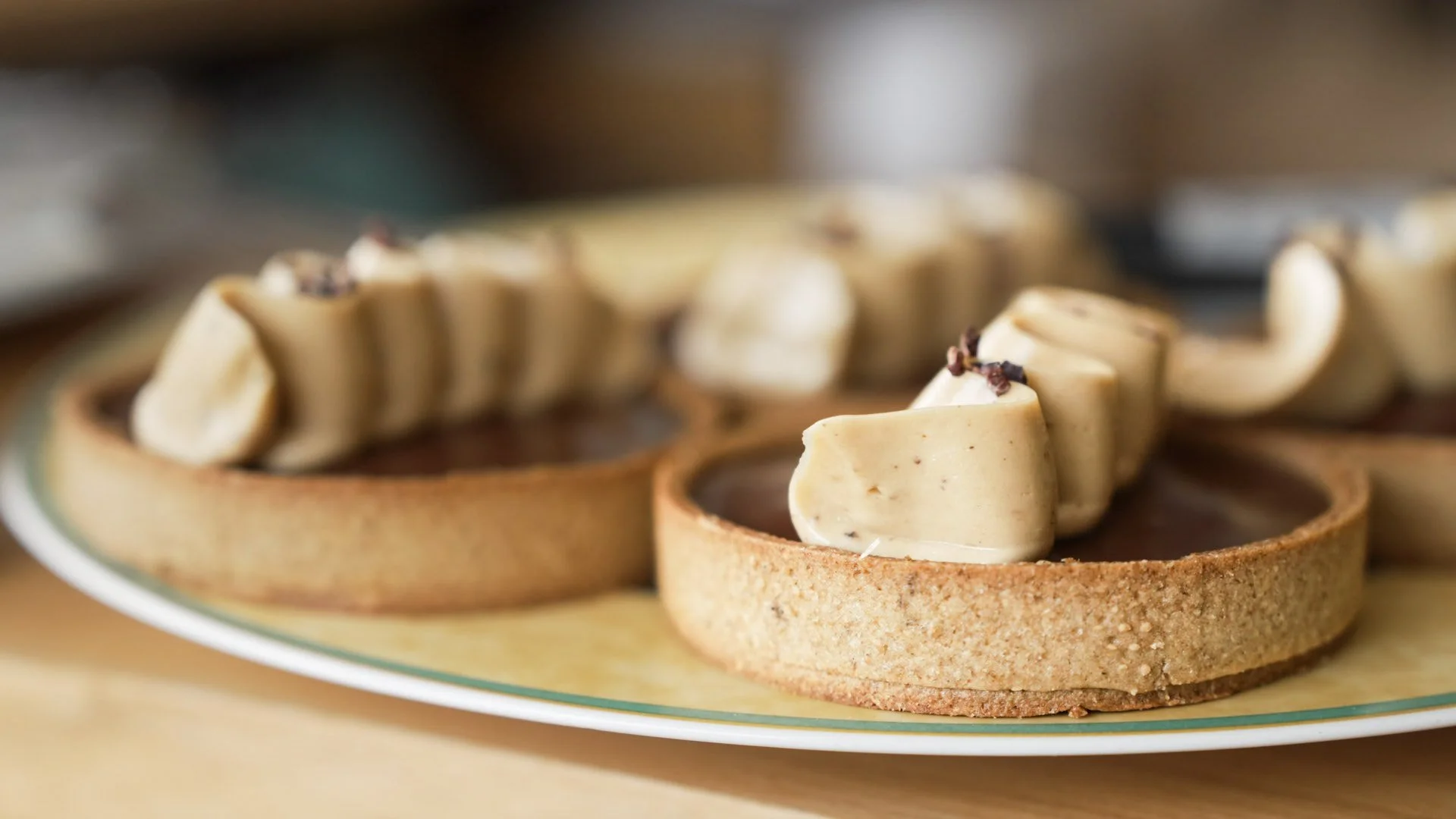 Close-up of tart shells filled with a creamy filling and garnished with chocolate shavings on a glass plate.