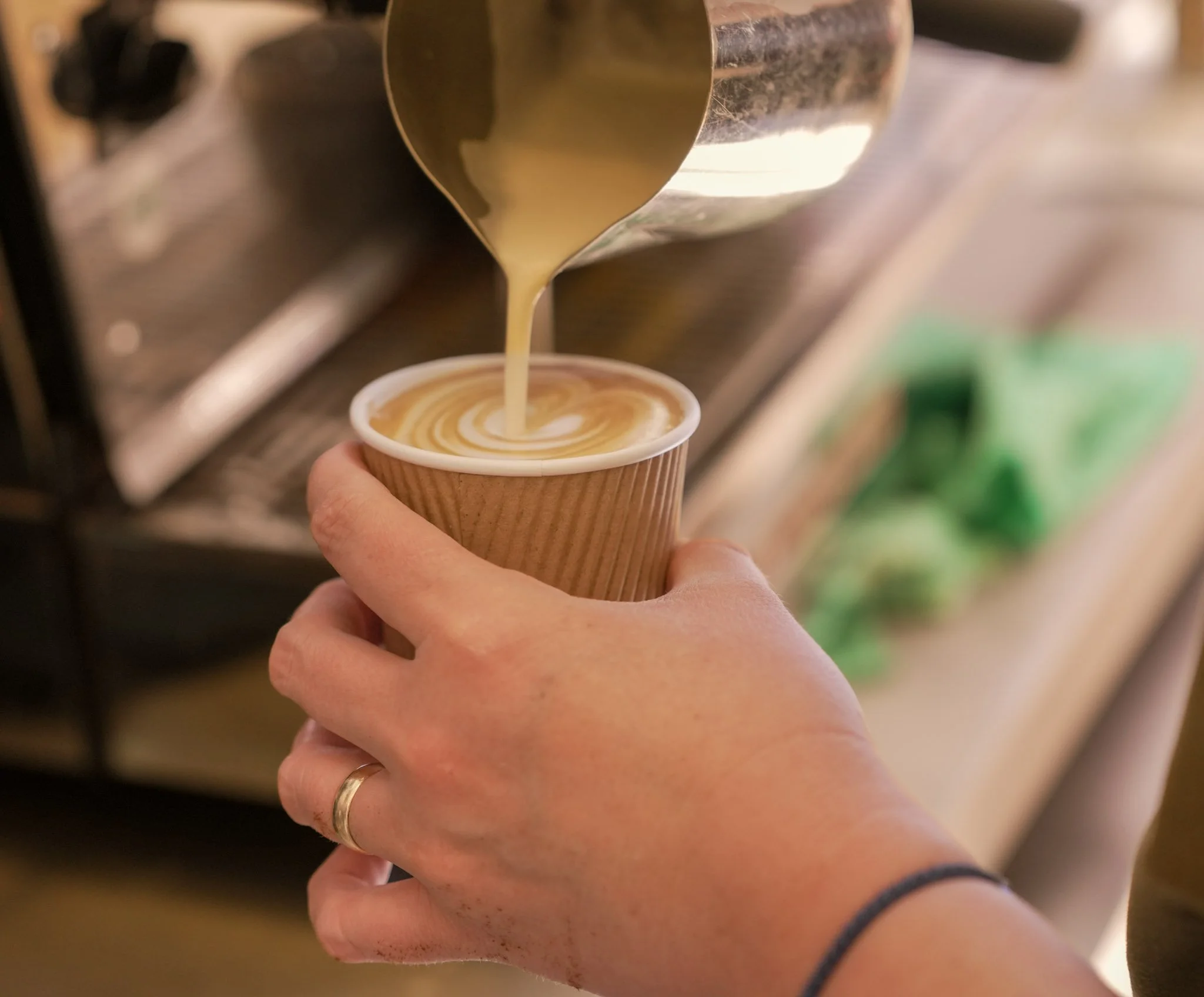 Hand pouring coffee into a paper cup with a swirl design