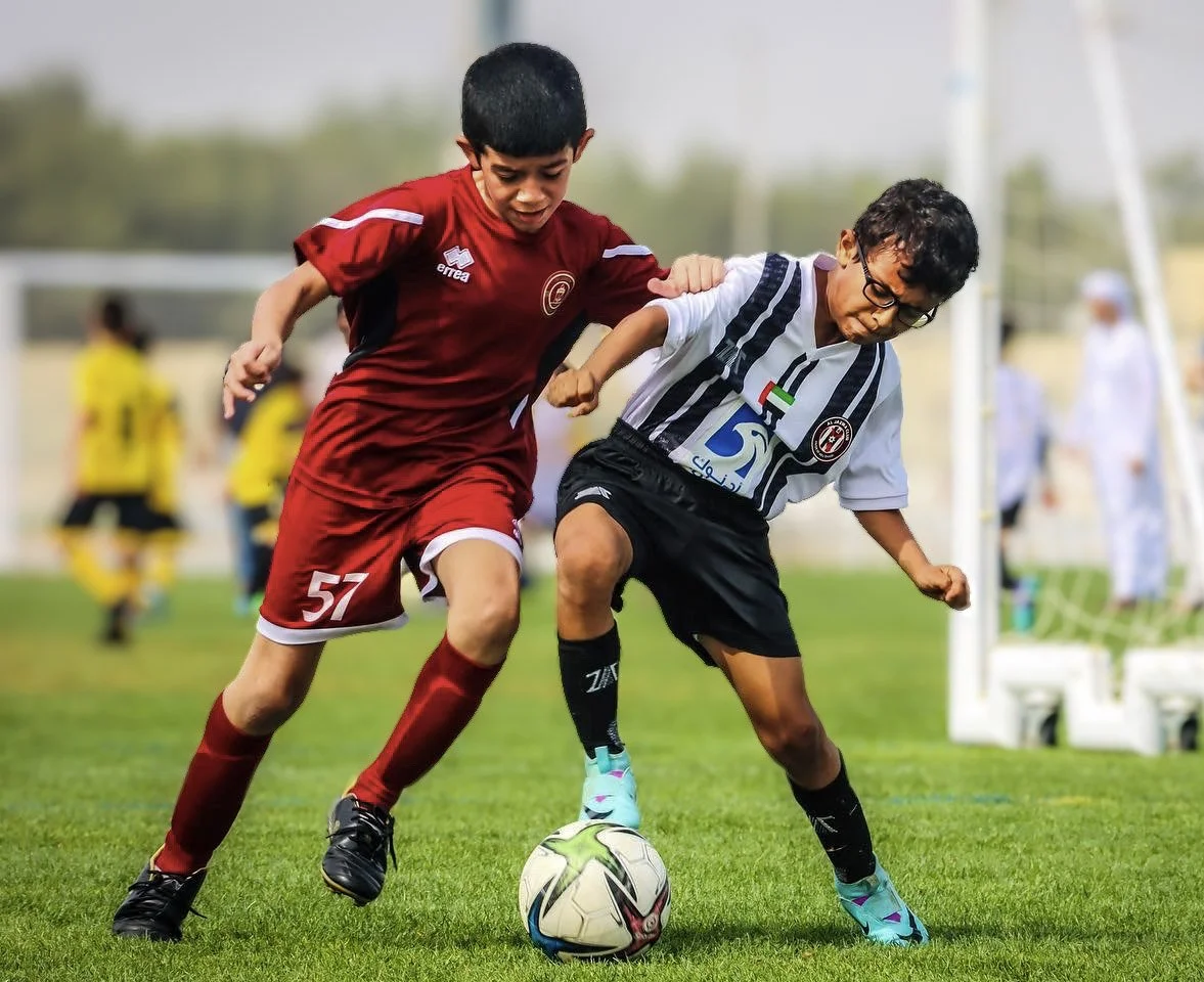 Two young boys play soccer on the field, fighting for possession of the ball during a match.