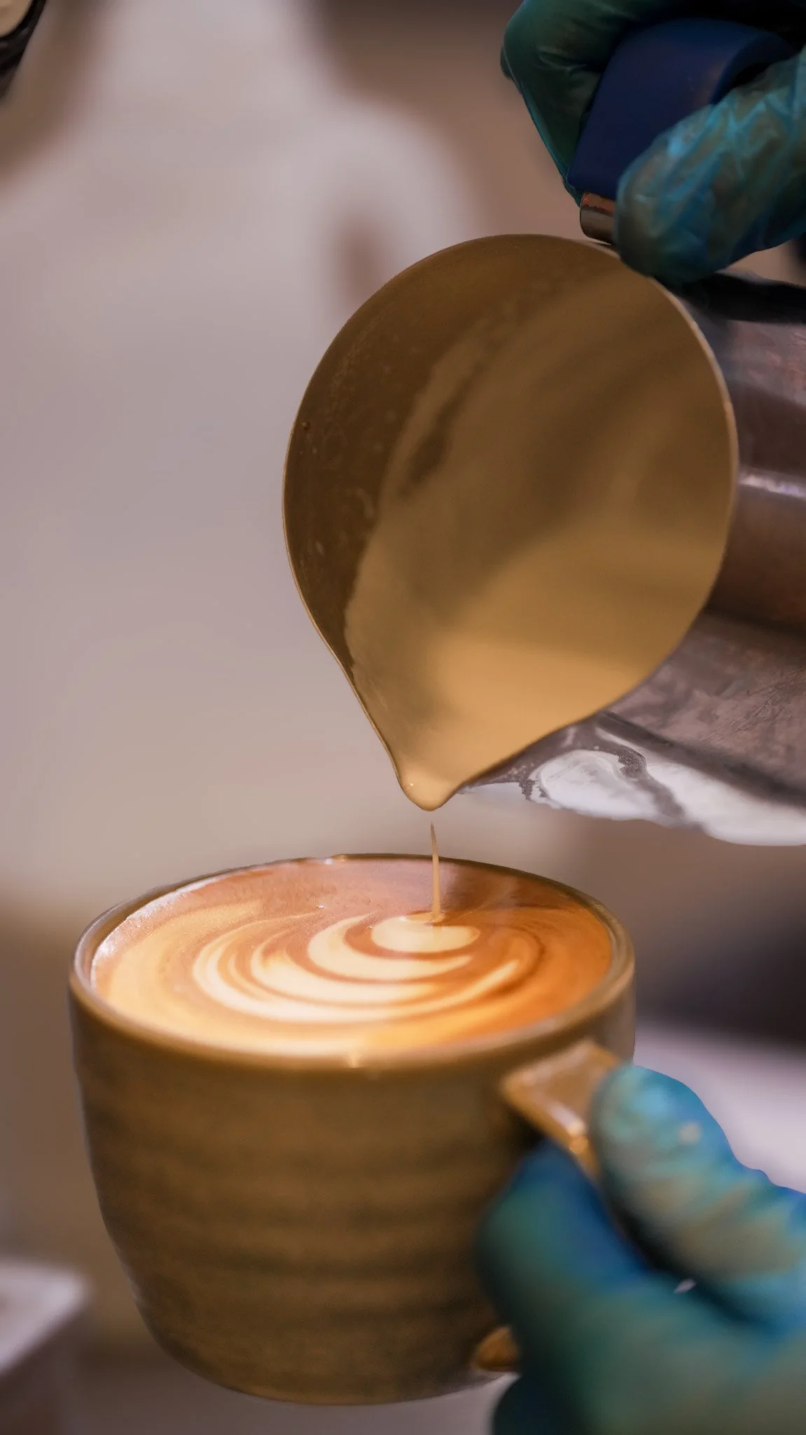Close-up of a barista pouring steamed milk into a cup of espresso to create latte art with a spiral pattern.