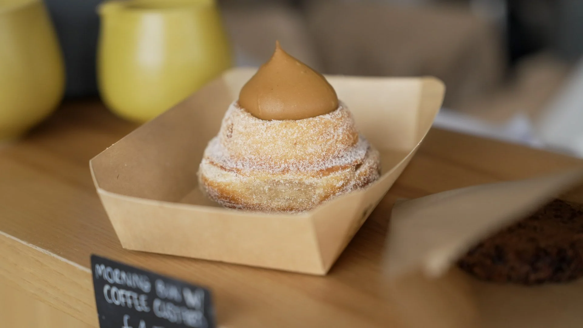 A cupcake with white powdered sugar on top and a dollop of caramel frosting, served in a small paper tray.