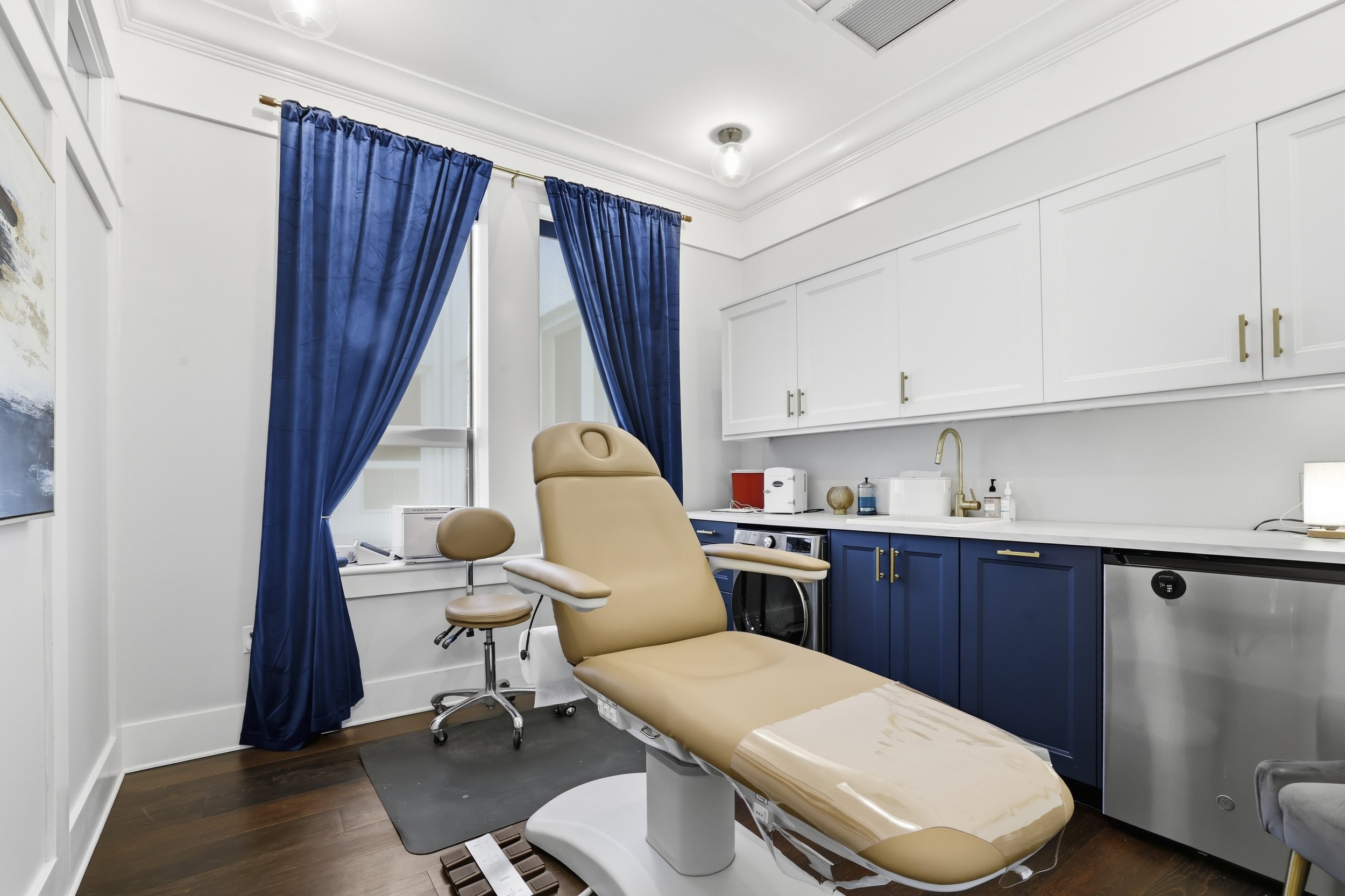 Dr. Harris' examination room with a beige medical chair, blue curtains, assorted cabinets, and medical supplies on the countertop