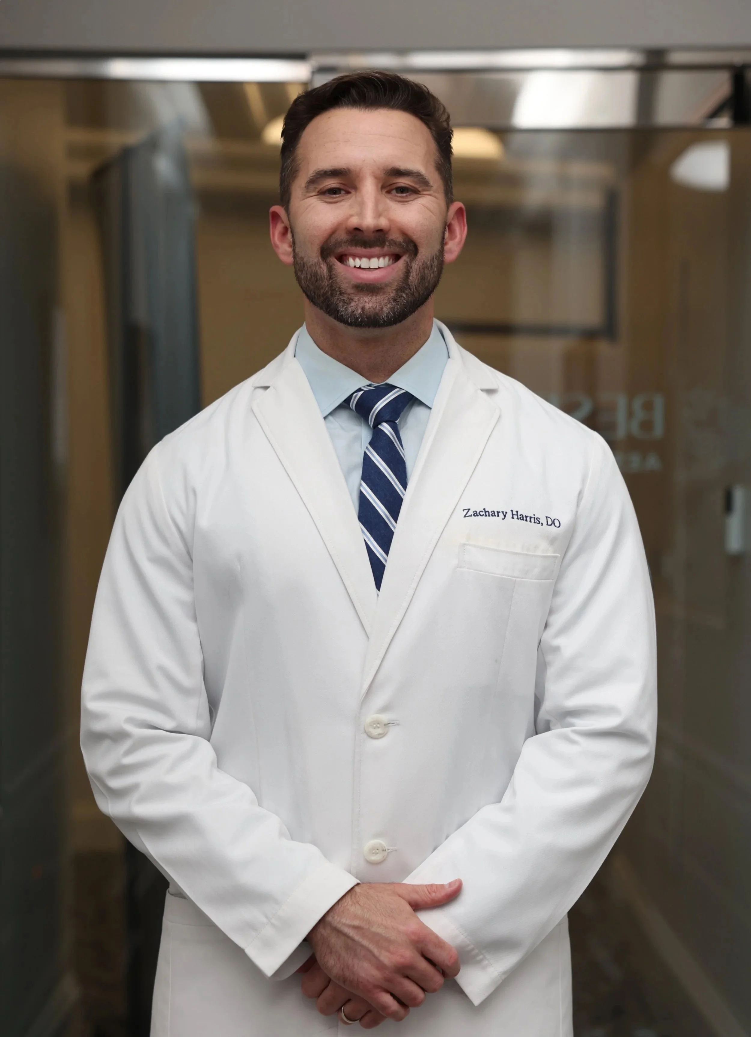 Dr. Zachary Harris smiling and posing in his white doctor's coat for a professional photo