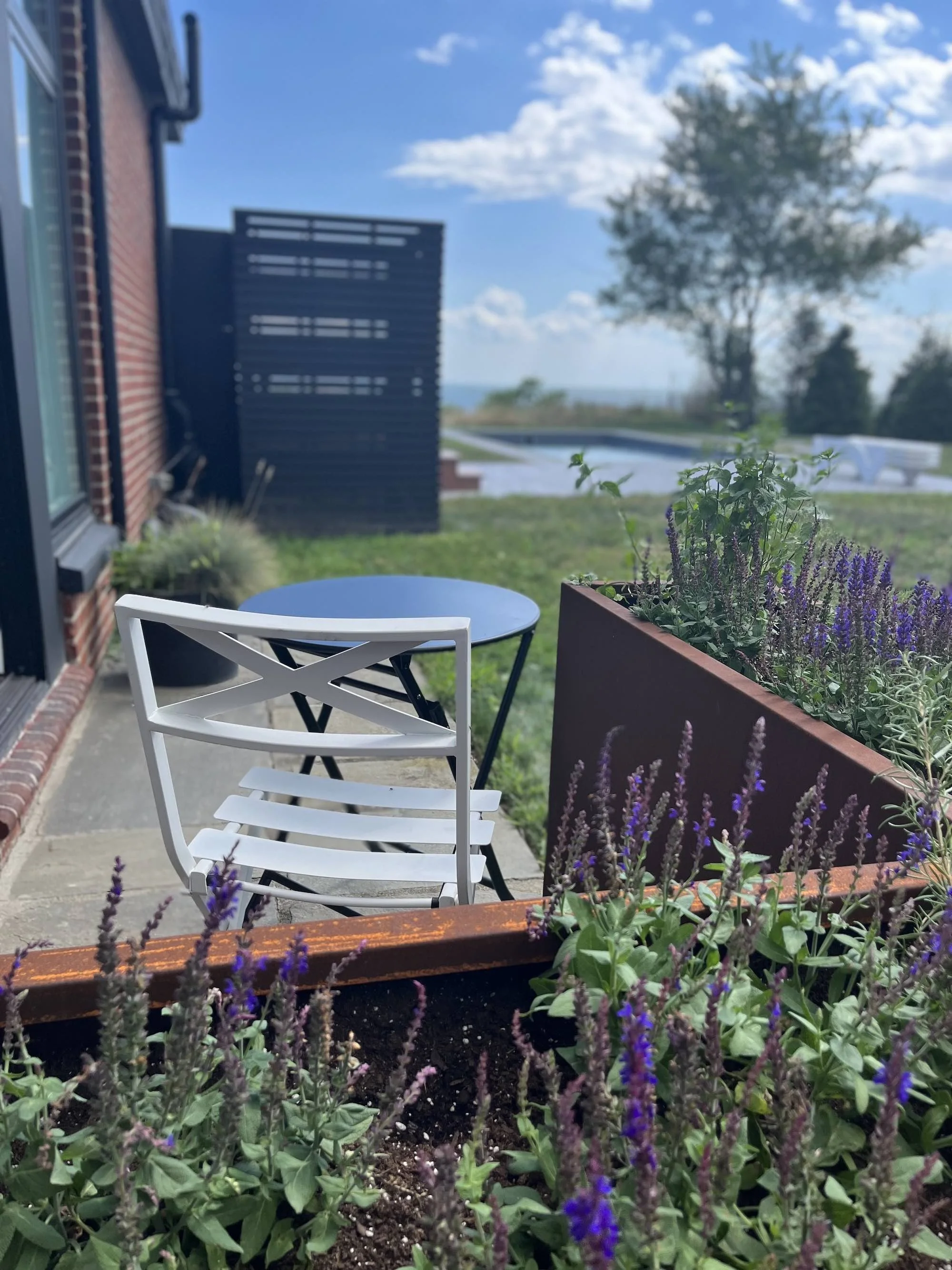 photo of the Fellow's patio with writing table and chair; view of pool and Long Island Sound beyond. In foreground, purple salvia rises from a planter