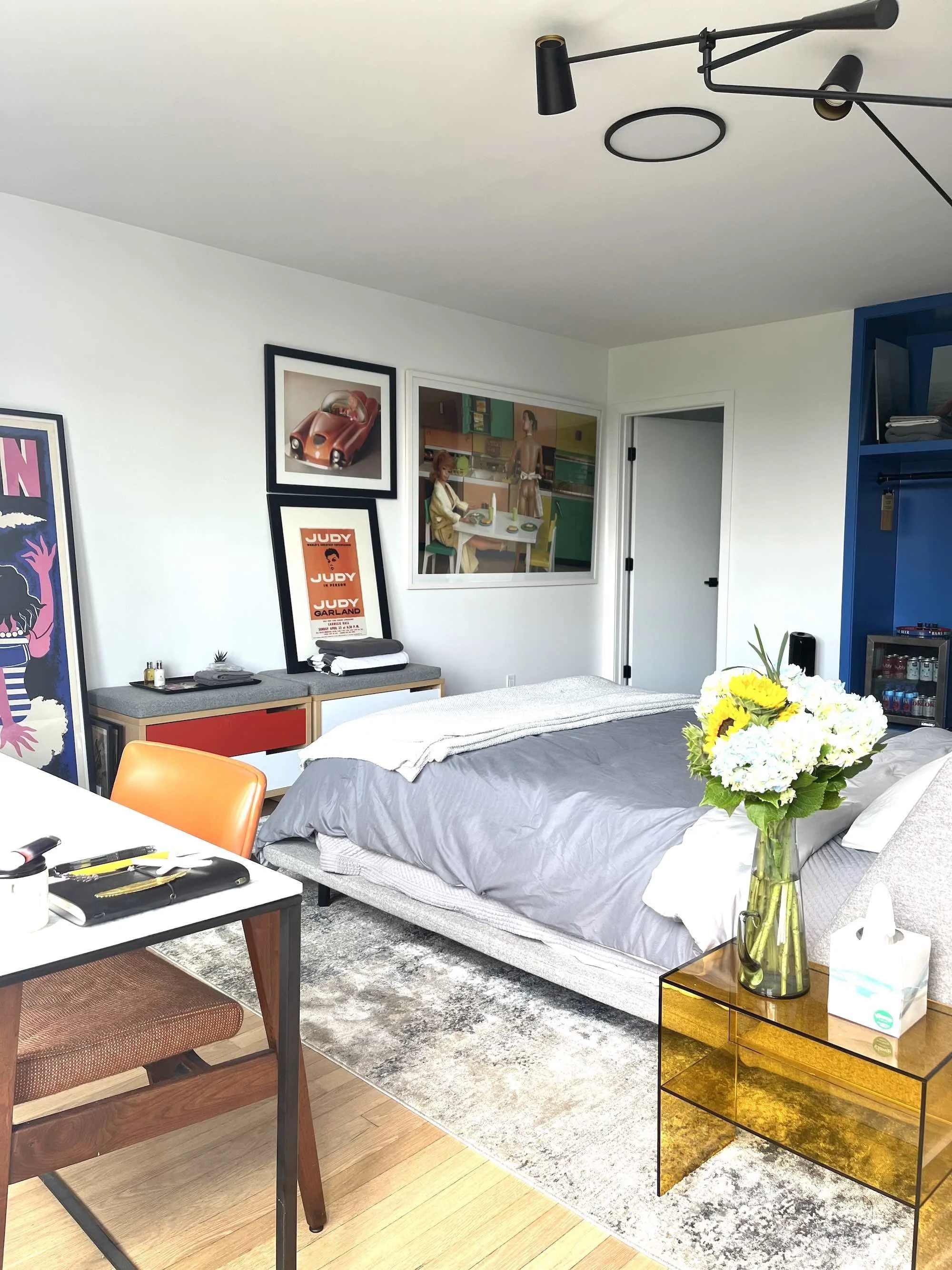 photo of Fellow's quarters (bedroom) with queen bed, writing desk; a fresh bouquet of hydrangea and sunflowers sits on the nightstand.