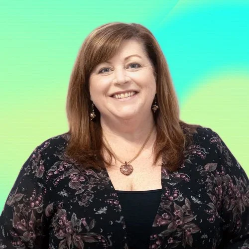 A smiling woman with shoulder-length auburn hair, wearing a black blouse with a celestial pattern, gold jewelry, and purple earrings, against a pink and purple gradient background.