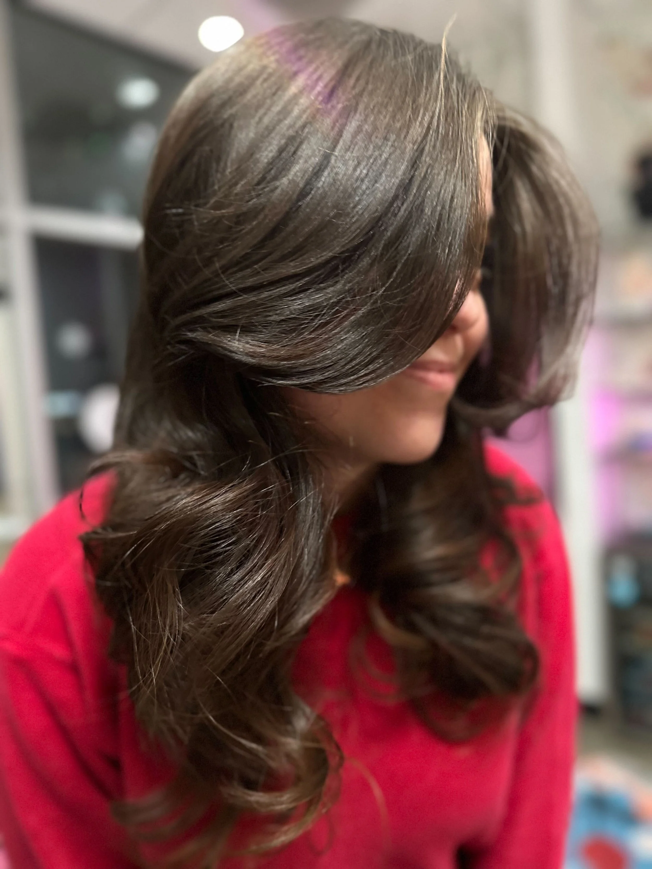 A woman with curly pink hair, topless, with a row of flowers around her waist and her arms raised above her head against a plain background.