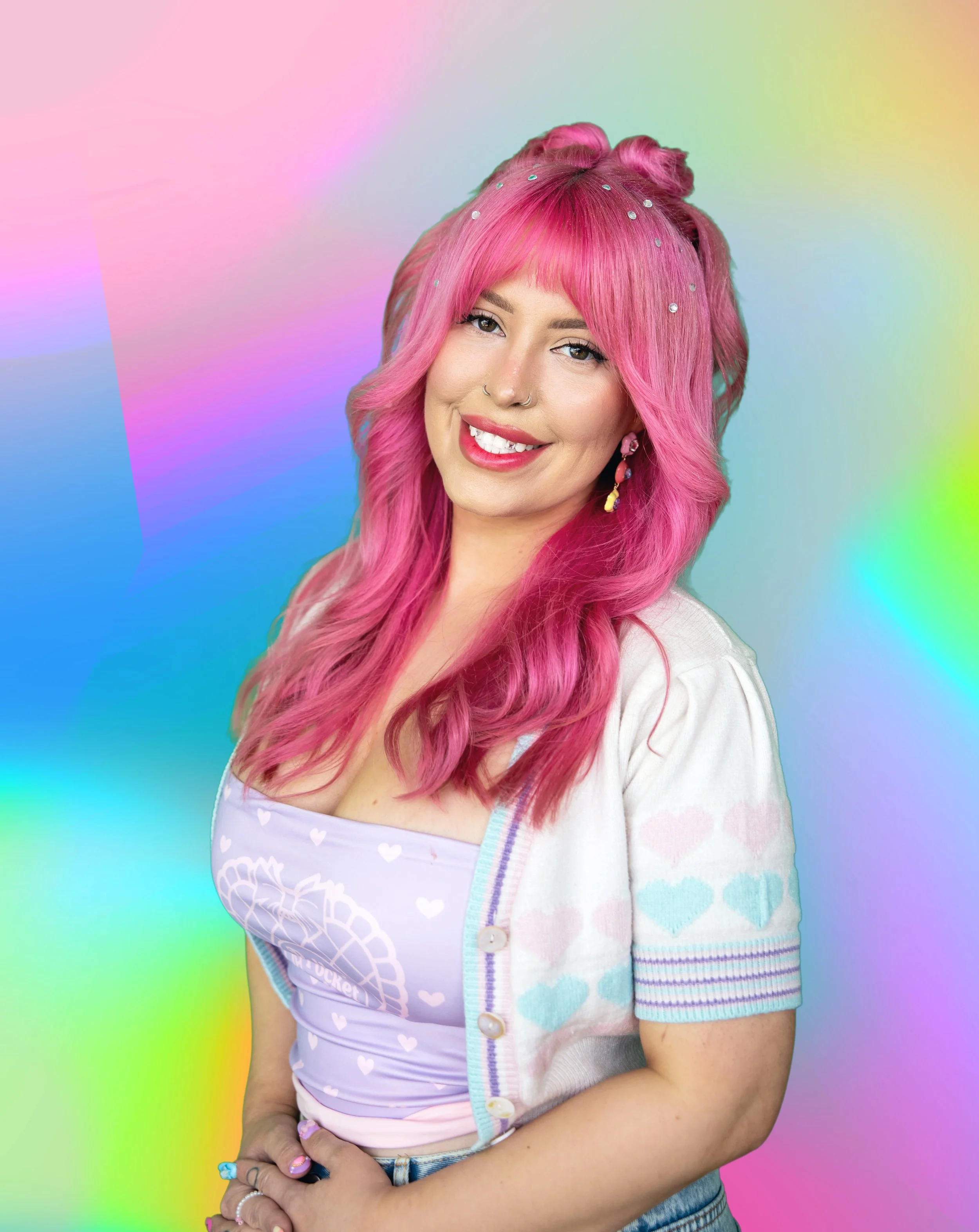 A woman with long, wavy hair that has multi-colored highlights, wearing a purple sleeveless top with small flower embellishments, posing against a colorful background.