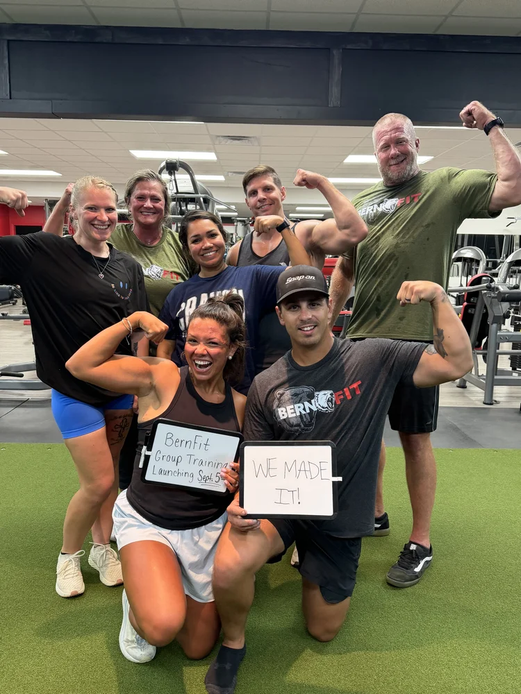 Group training members flexing and holding signs after a class at Bern Fit