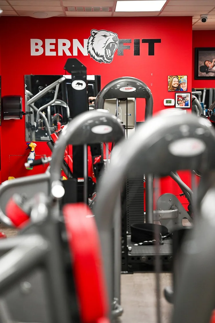 Weight machines in front of a red wall with the Bern Fit logo