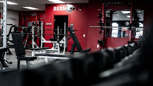 Squat rack and barbell in front of a red wall with the Bern Fit logo