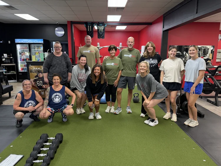 Group fitness class posing on the turf in front of the red wall at Bern Fit