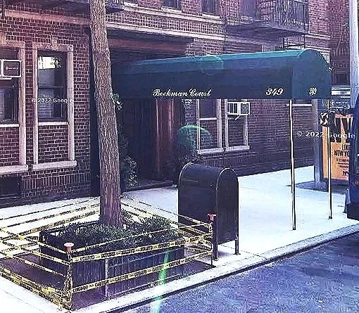 City sidewalk with brick building, green tree, black mailbox, and blue awning reading 'Beekman Court' with numbers 349 and 345.