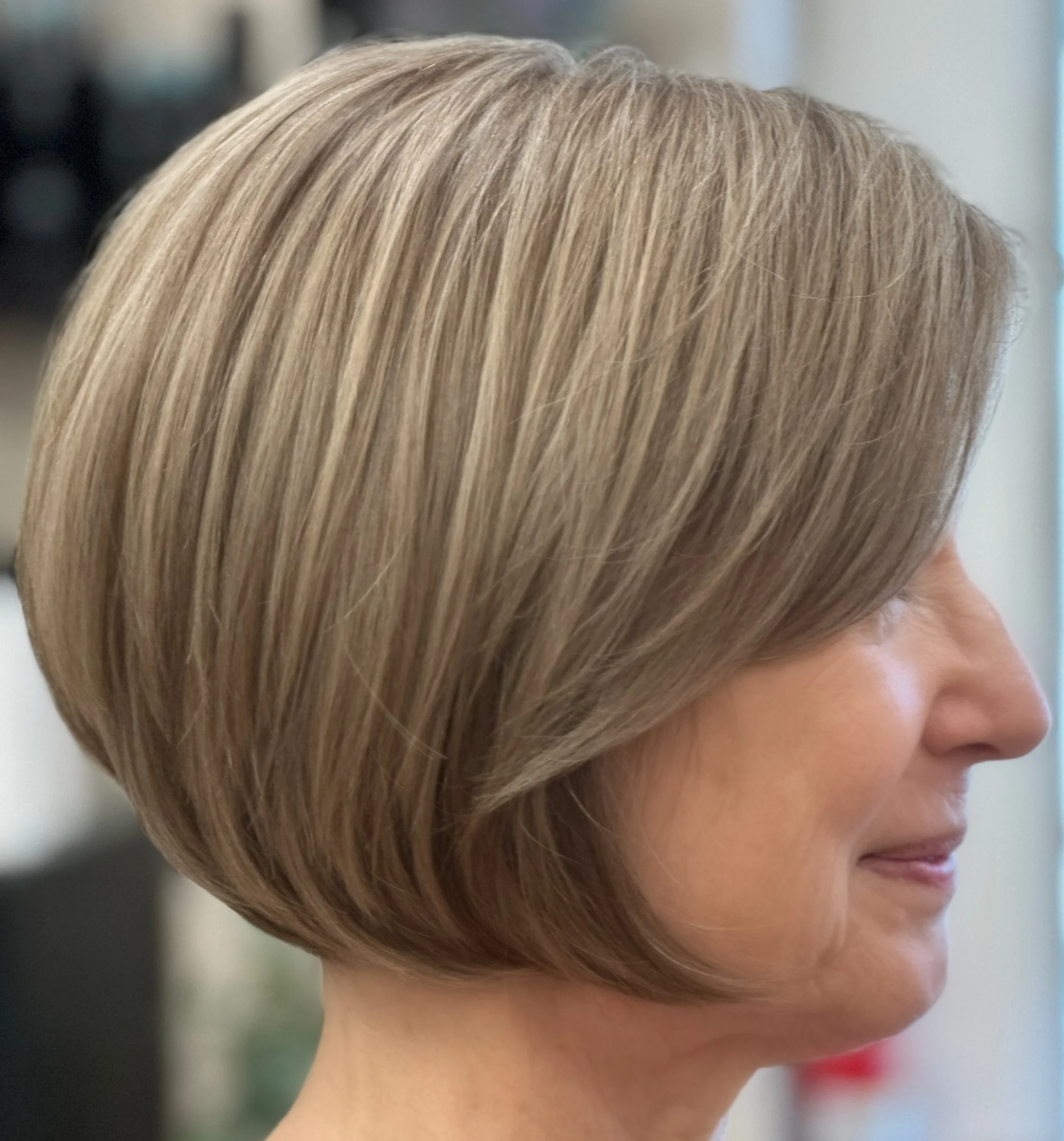 Close-up of a woman's short, layered haircut, viewed from the side, showcasing smooth, light brown hair.