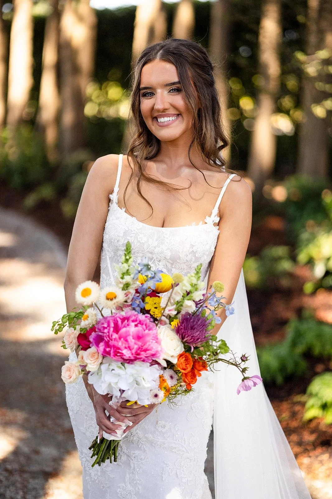 A young woman in a white wedding dress holding a colorful bouquet of flowers outdoors.