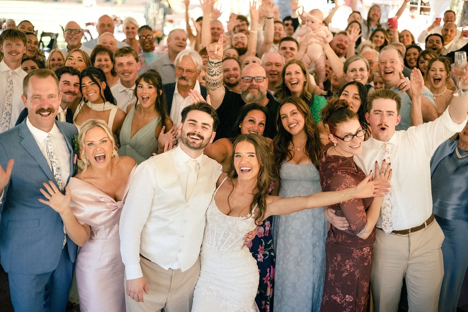 A large group of people celebrating at a wedding, smiling and posing for a photo in a festive setting.