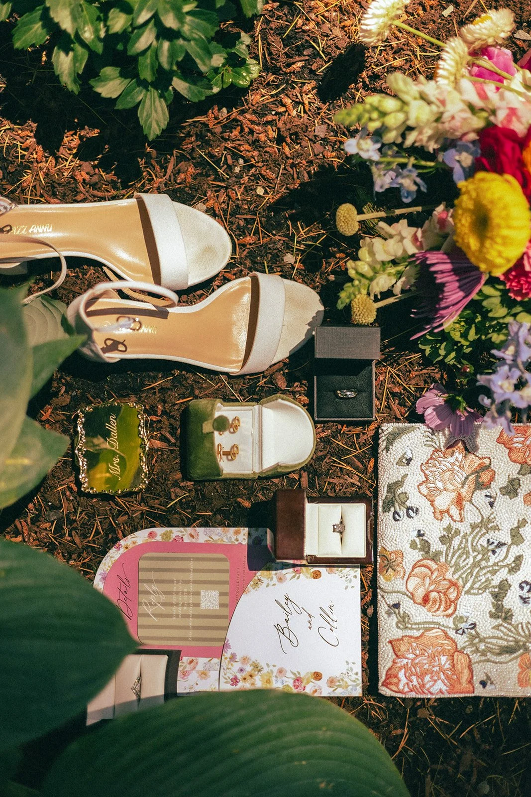A memorial on the ground with flowers, jewelry, rings, and greeting cards placed among greenery.