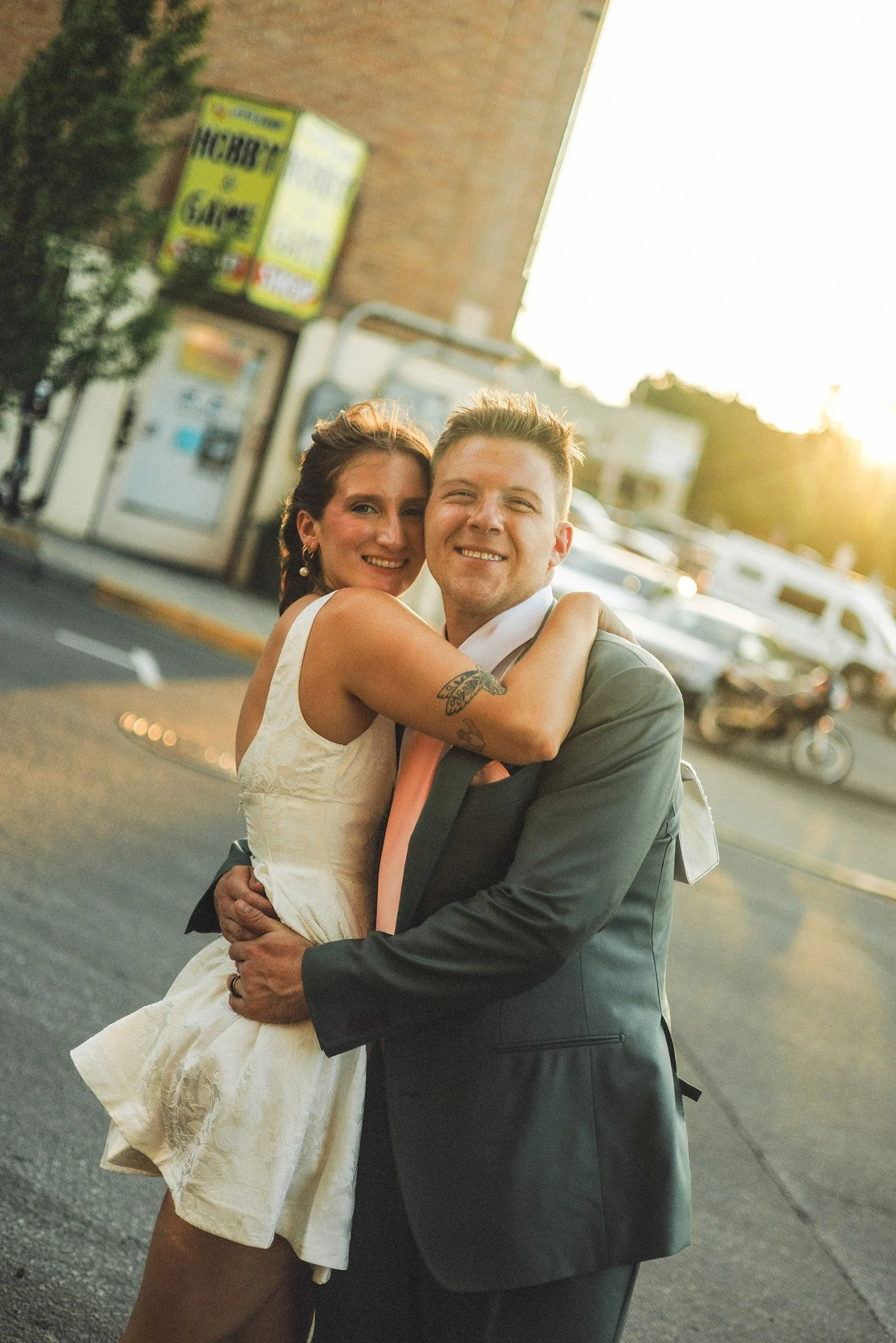 A happy couple in formal attire hugging on a city street at sunset.