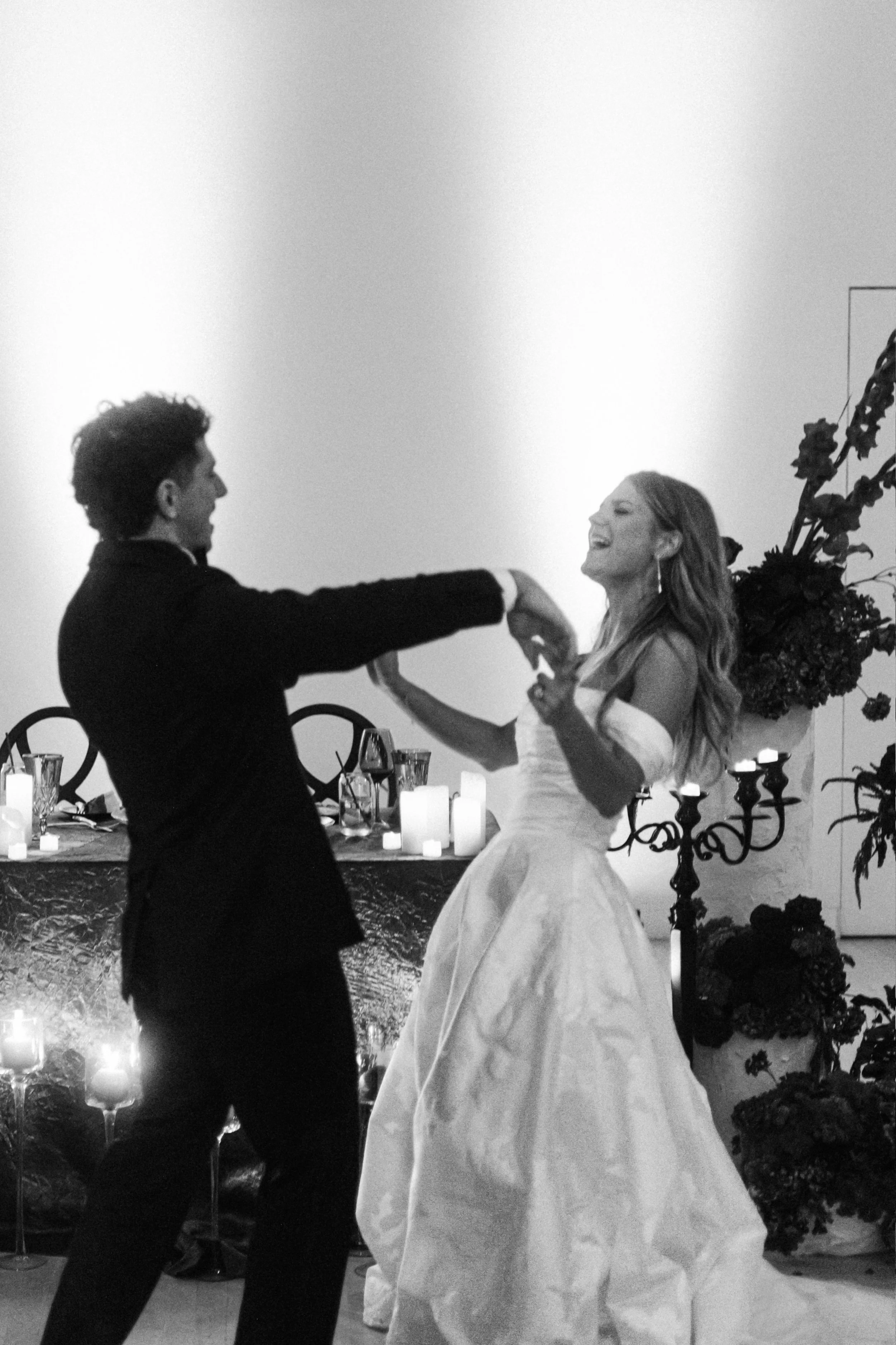 A man and a woman in wedding attire dancing at a wedding reception, with candles and floral decorations in the background.
