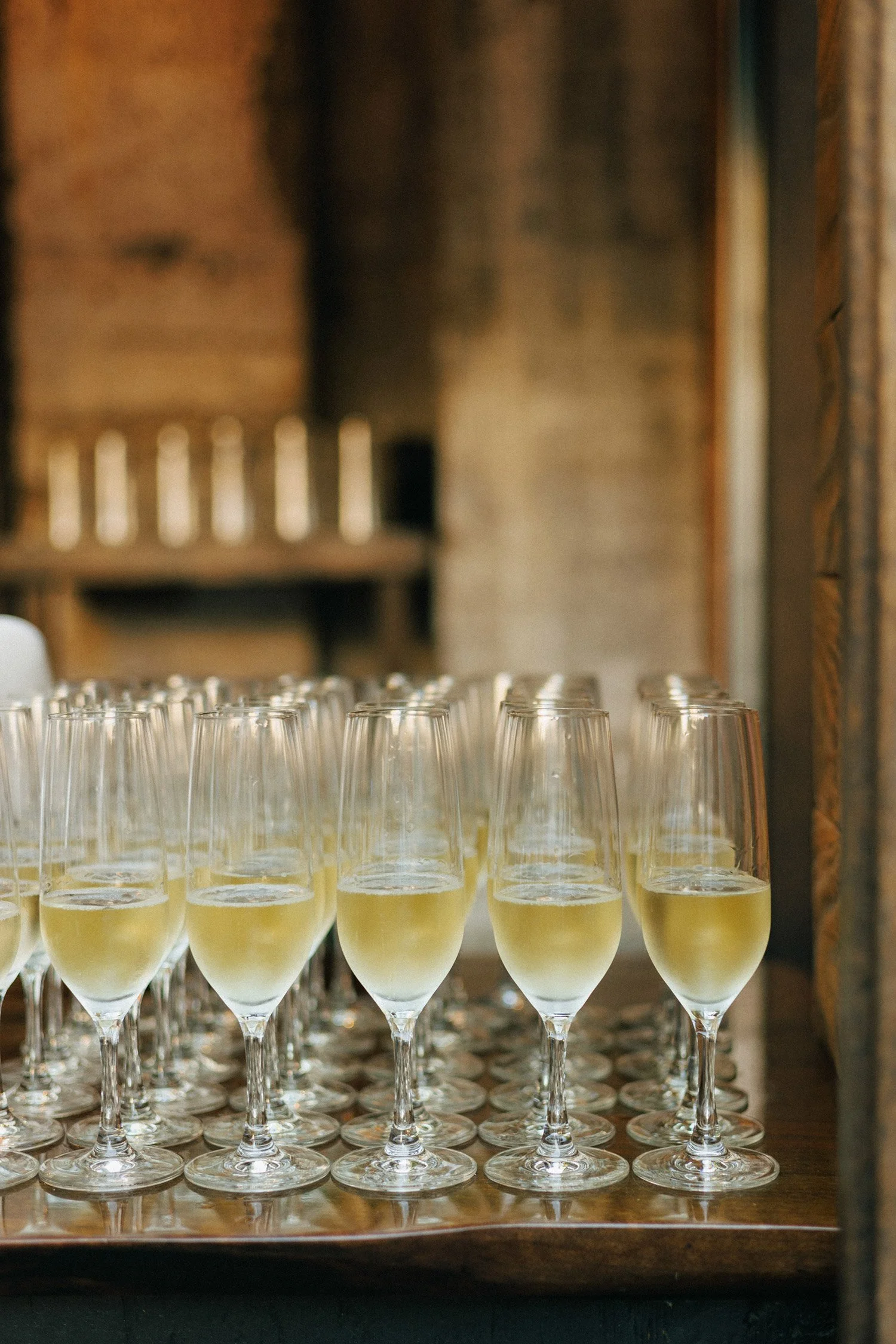 Multiple glasses of white wine on a wooden table, with a blurred background of a rustic interior.