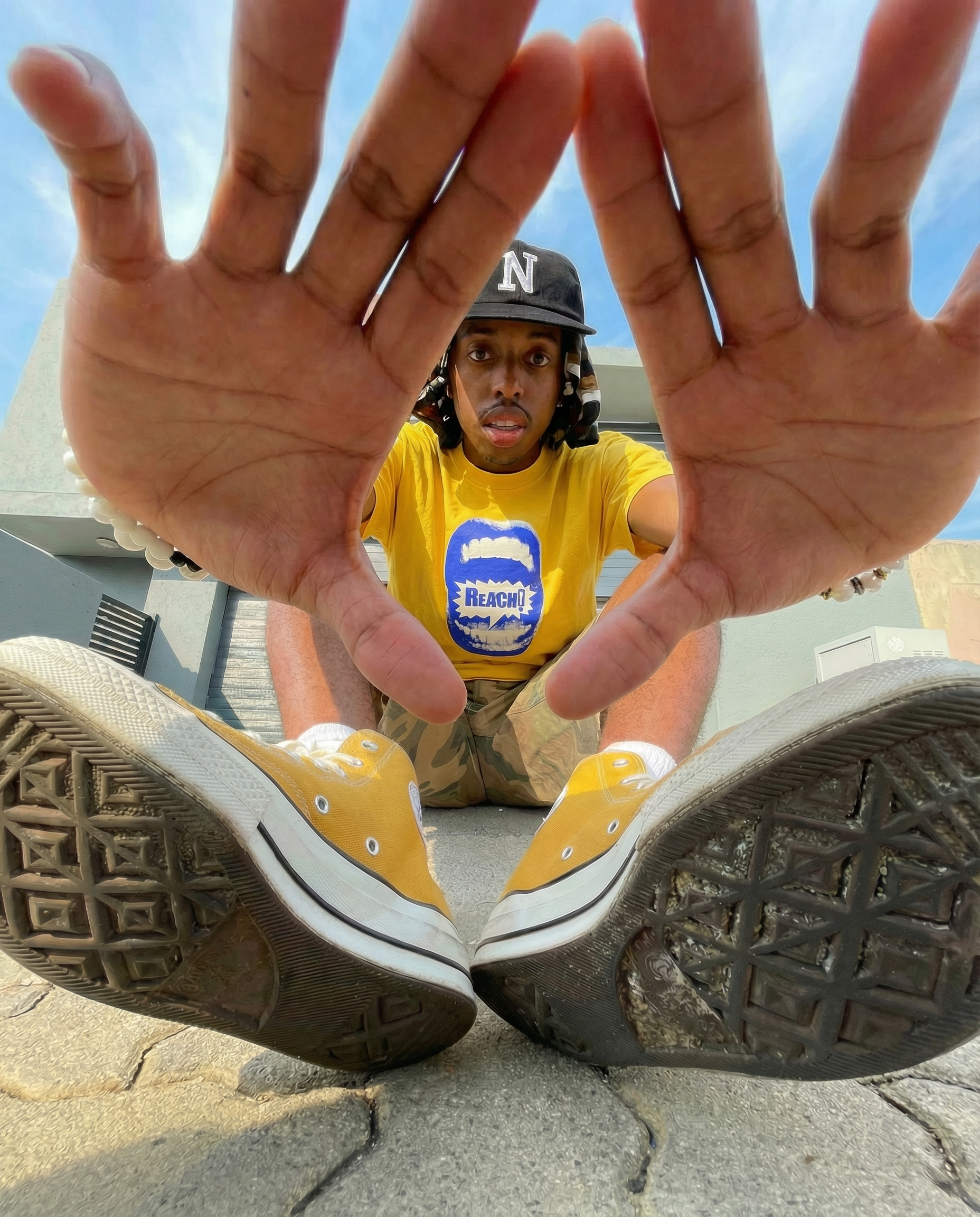 A person in a yellow shirt with a blue design is lying on the ground with their legs extended and shoes in the foreground. The person is looking directly at the camera.