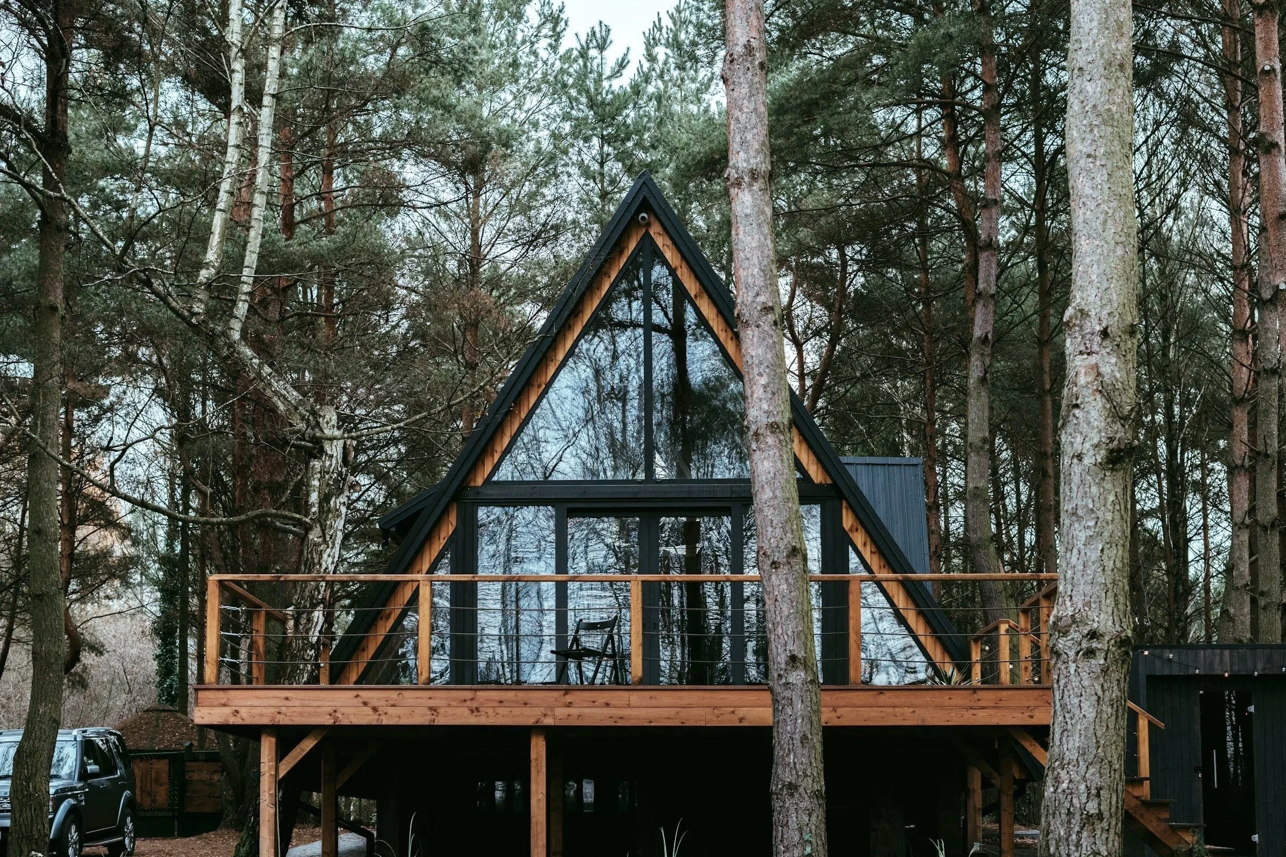 A modern A-frame house with large glass windows, surrounded by tall pine trees in a wooded area.