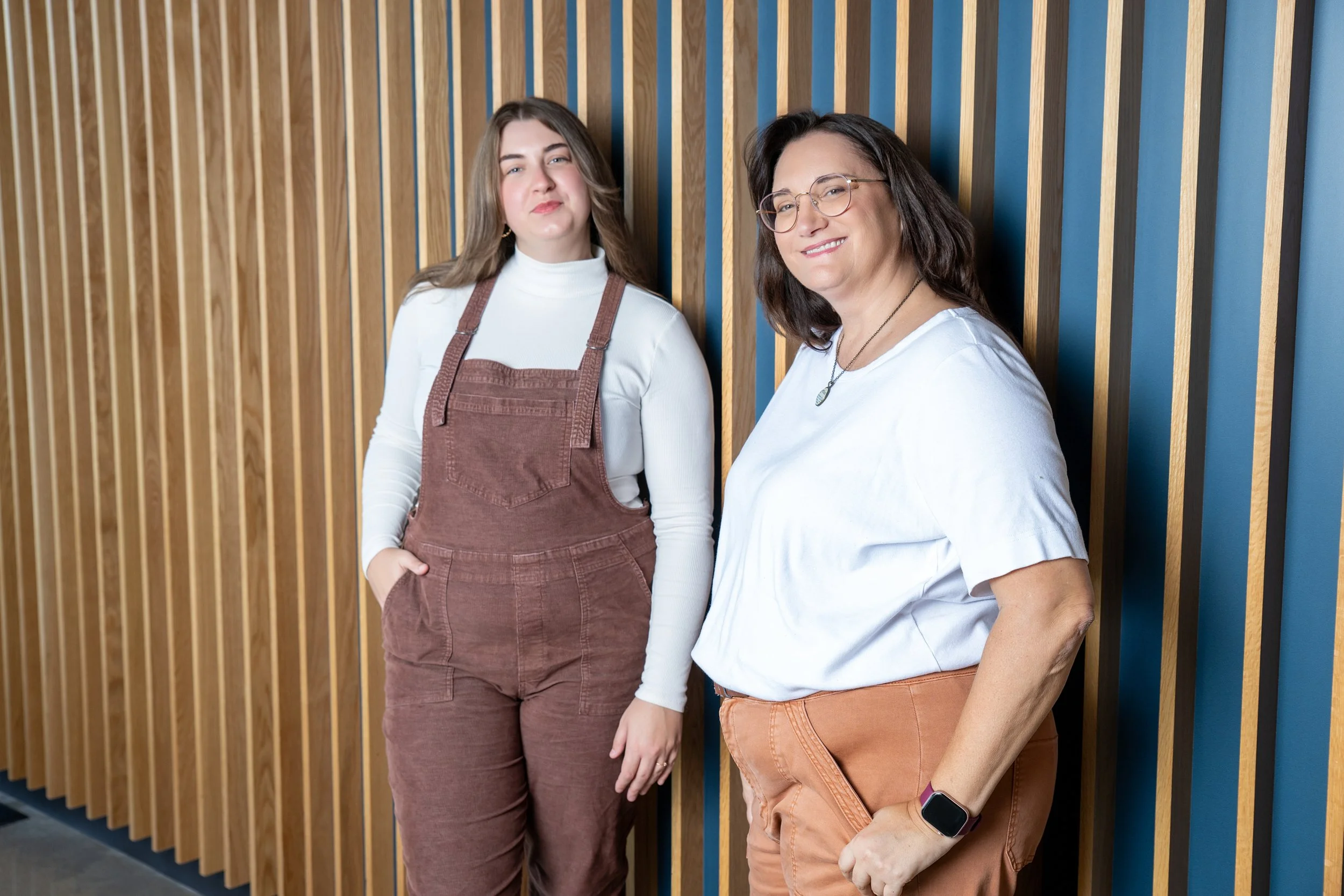 Cari Kaufman and Alex Andrews of Storyteller Wordsmith stand against a wall made of natural wood.