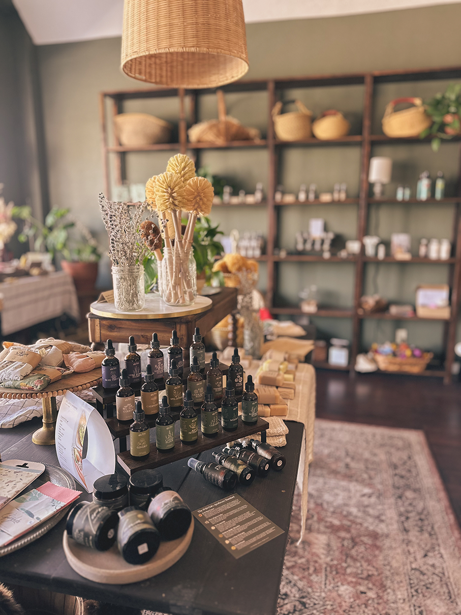 Display of tinctures and skincare products arranged on a table within a boutique shop, with shelves of baskets and other items in the background.