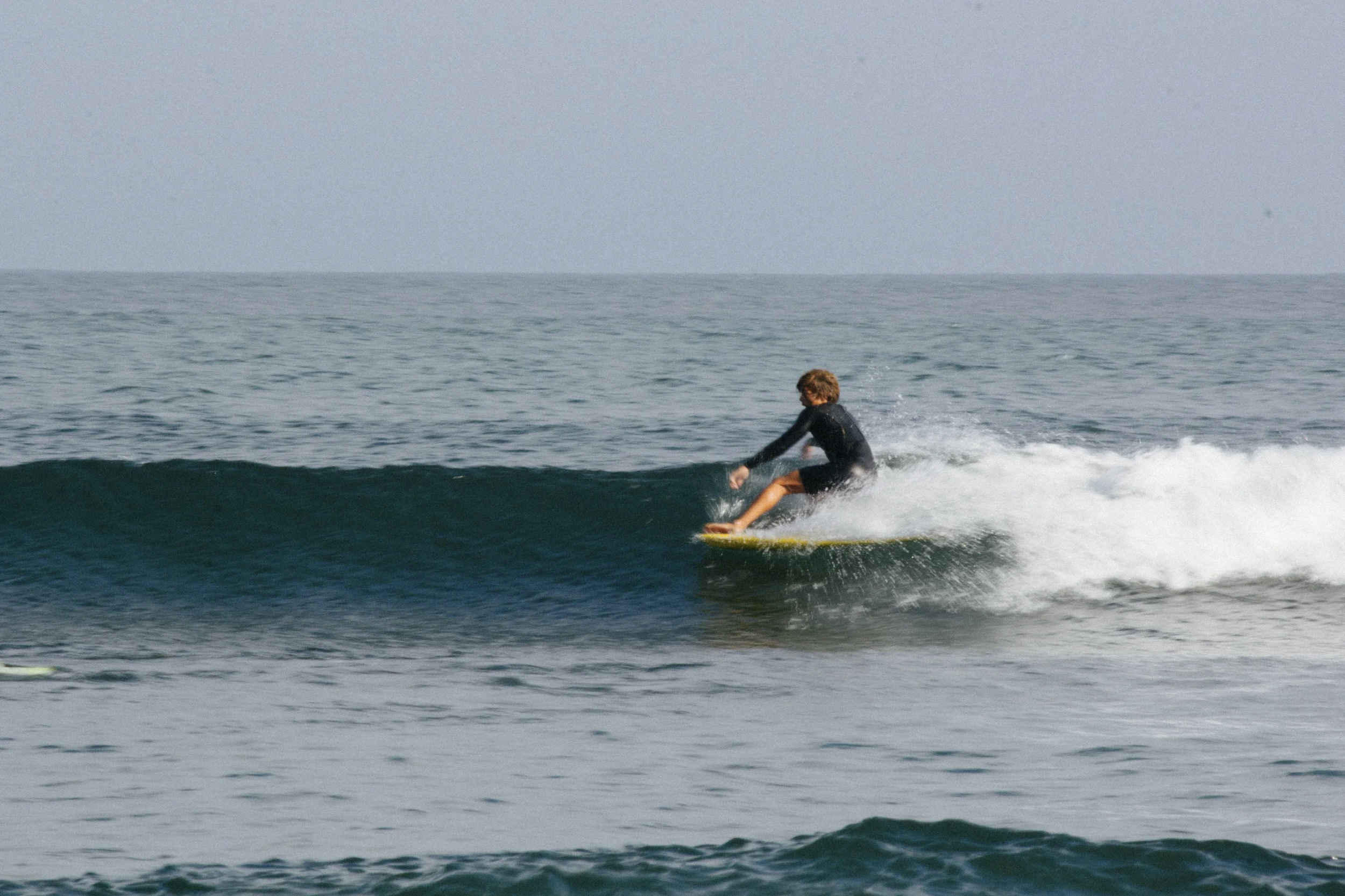 A person surfing on a small wave in the ocean, wearing a dark wetsuit.
