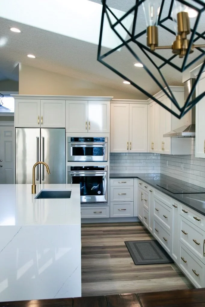 Calgary Renovation Contractor modern white kitchen with quartz waterfall island, gold fixtures, stainless steel appliances, and custom cabinetry.