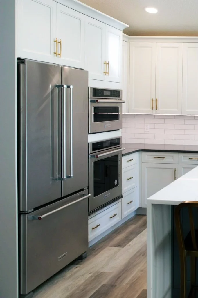 After kitchen renovation in Royal Oak Calgary with white shaker cabinets, quartz countertops, stainless steel appliances, and gold hardware.