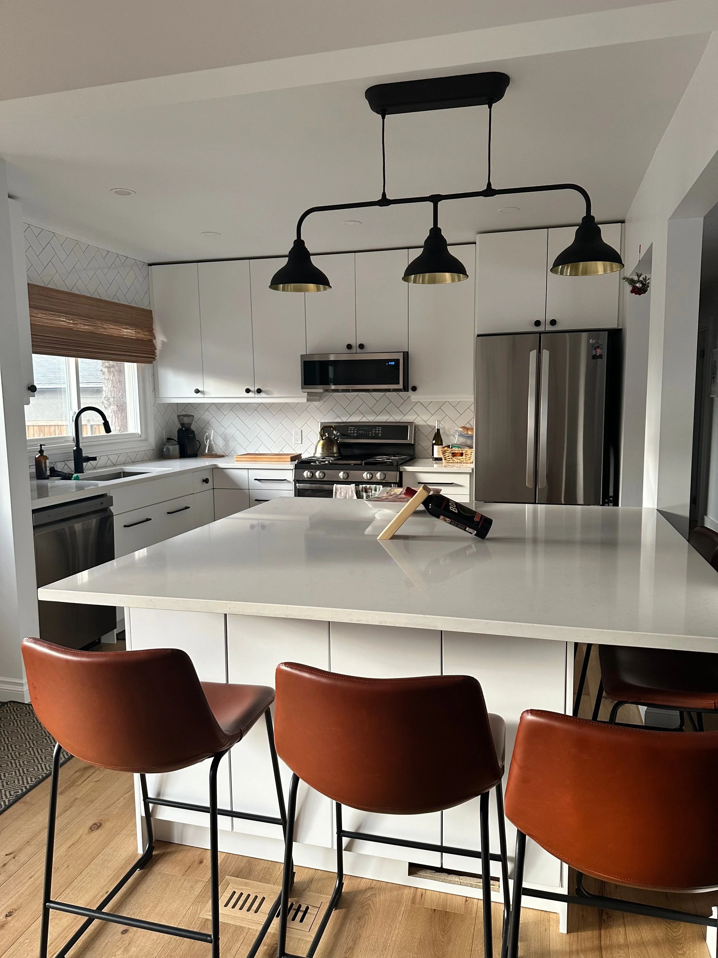 Calgary Renovation Contractor modern white kitchen with quartz island, custom cabinetry, stainless steel appliances, and stylish lighting