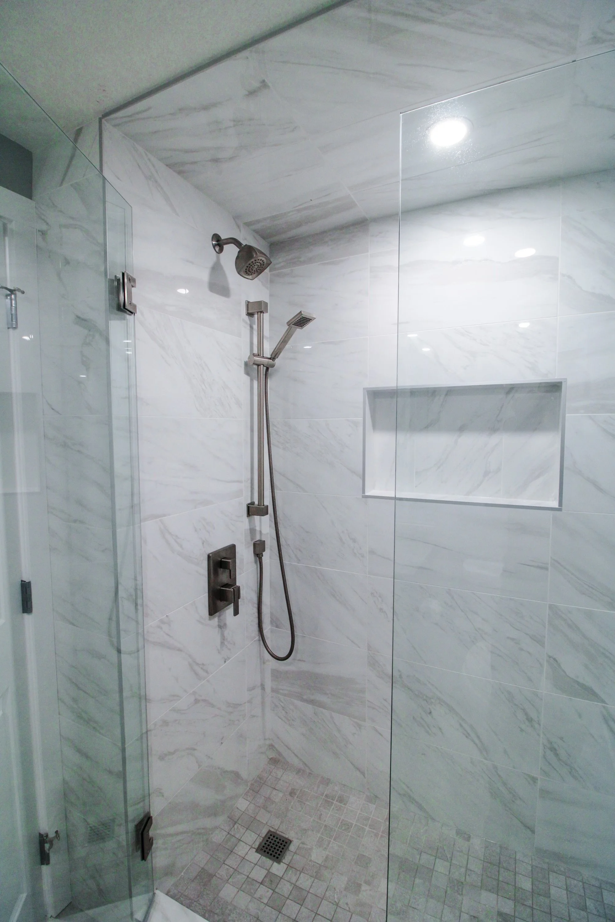Calgary Renovation Contractor luxury shower with marble-style tile, glass enclosure, rainfall showerhead, and built-in niche.
