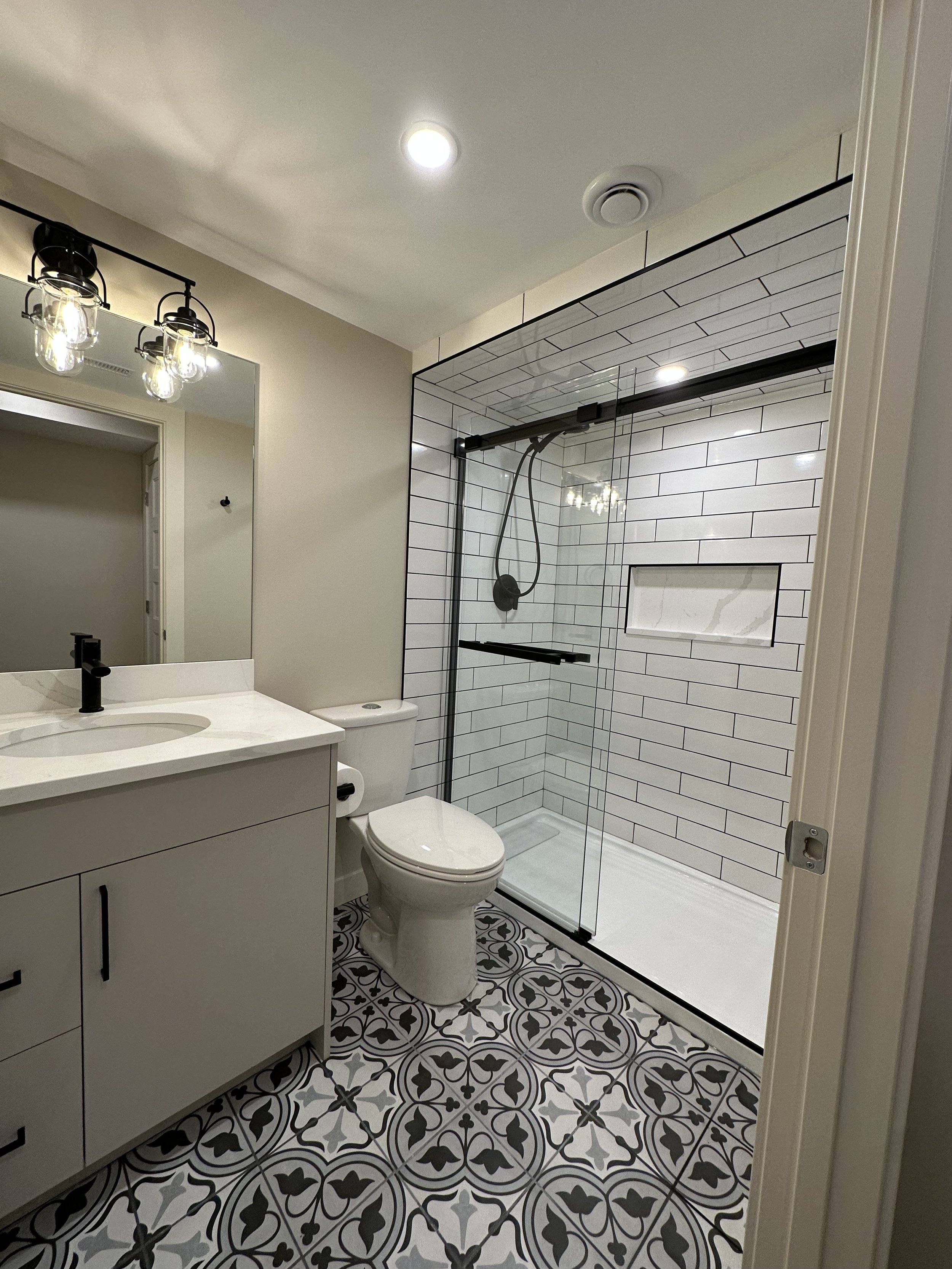 Calgary Renovation Contractor modern bathroom with patterned tile floor, glass shower, subway tile walls, and custom vanity.